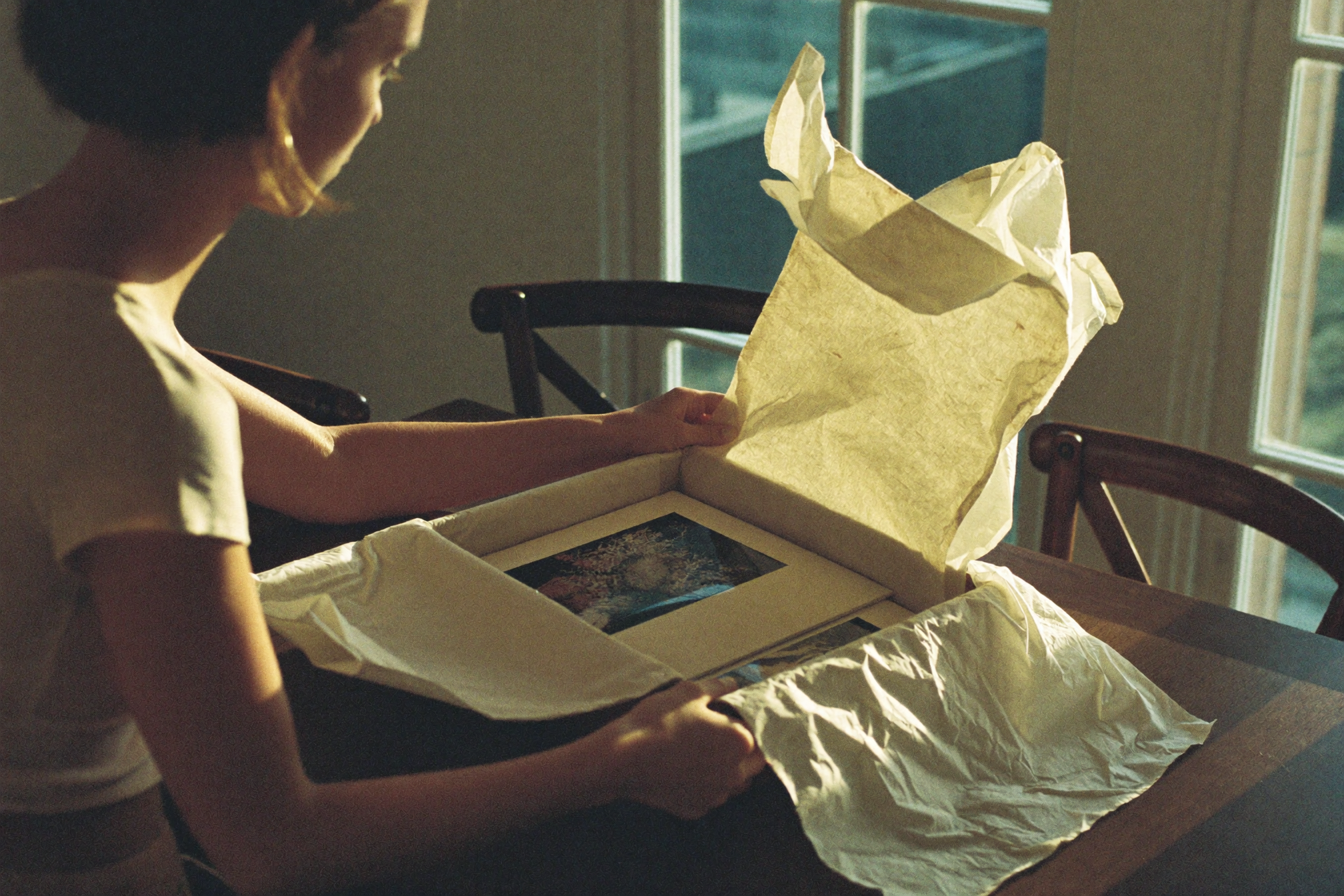 Hands opening a linen keepsake box revealing fine art prints in tissue