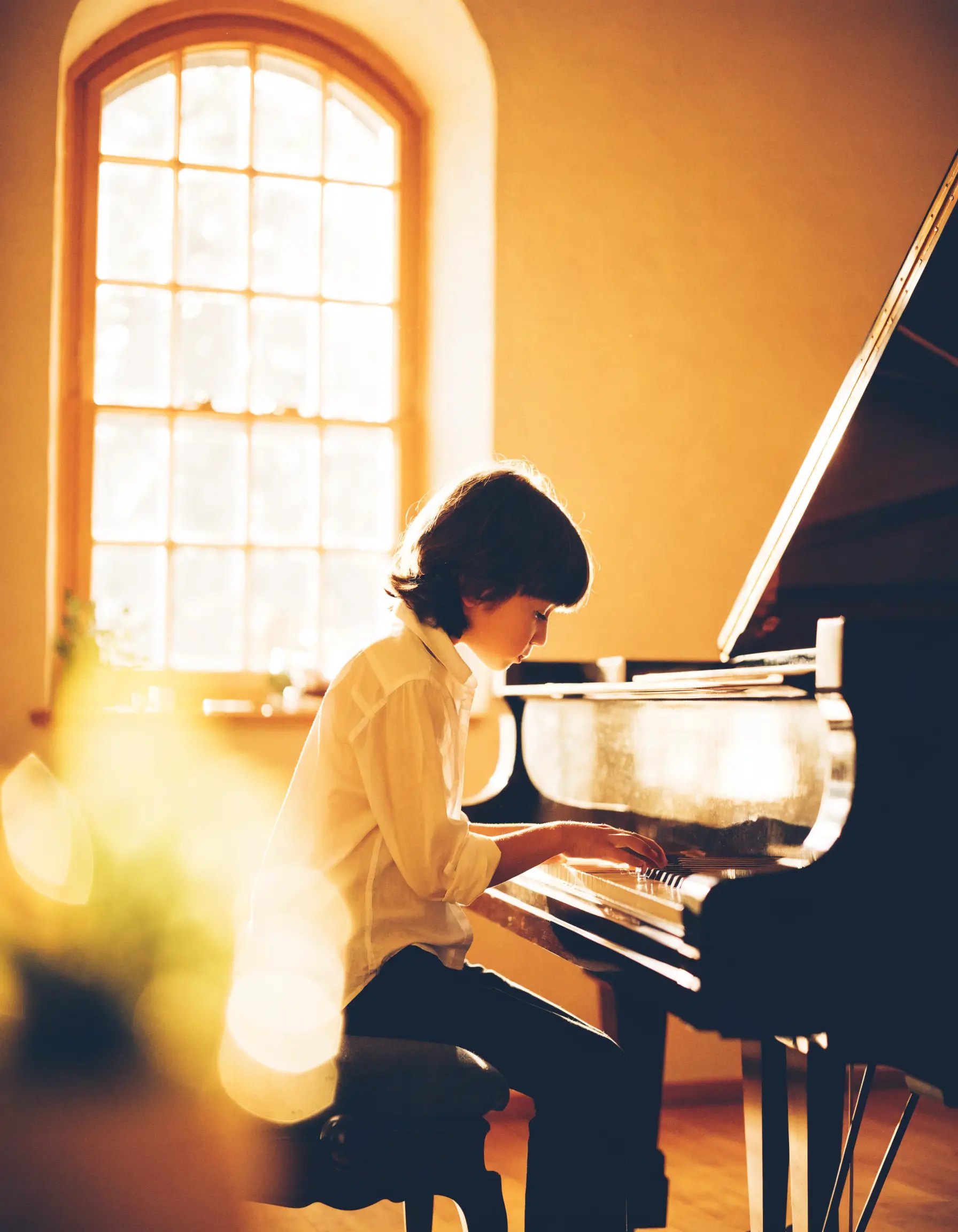 A young student playing the piano by a sunlit window