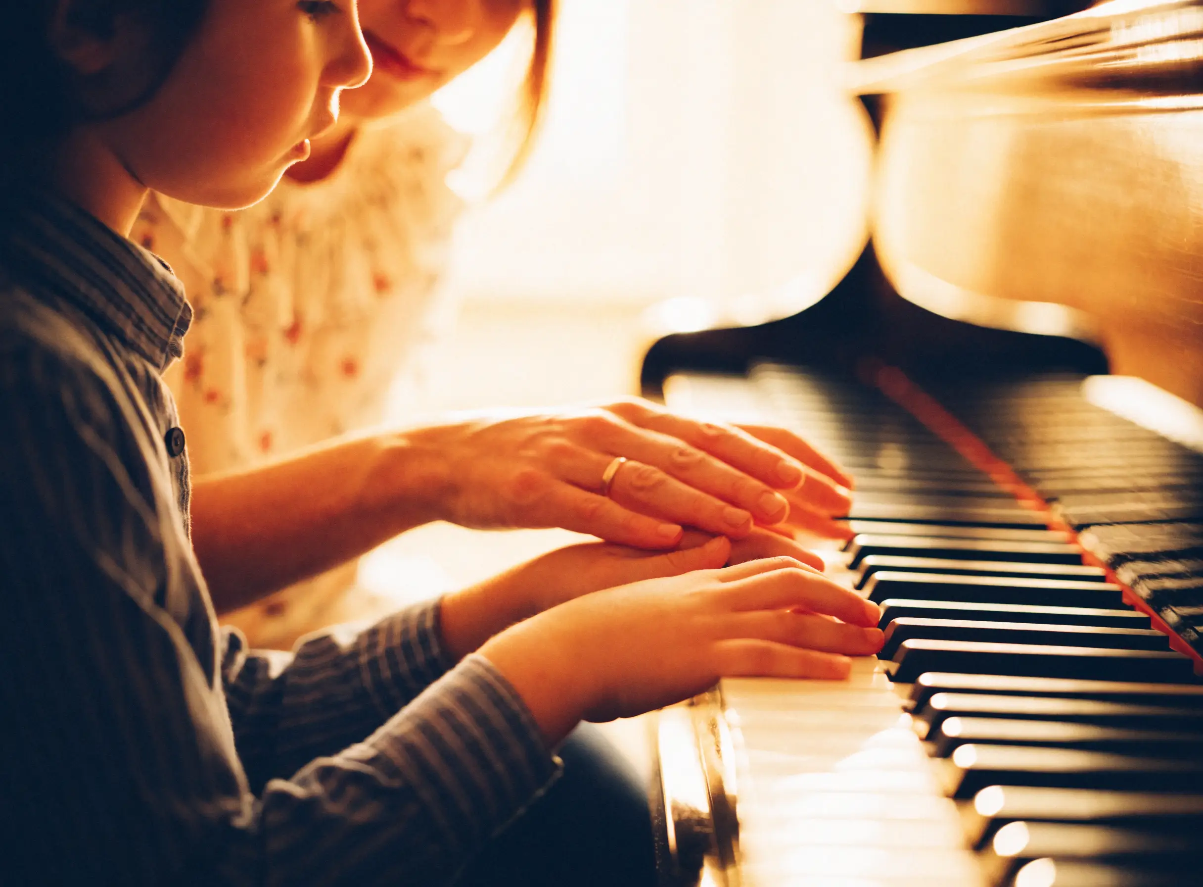 A teacher gently guiding a young student's hands at the piano