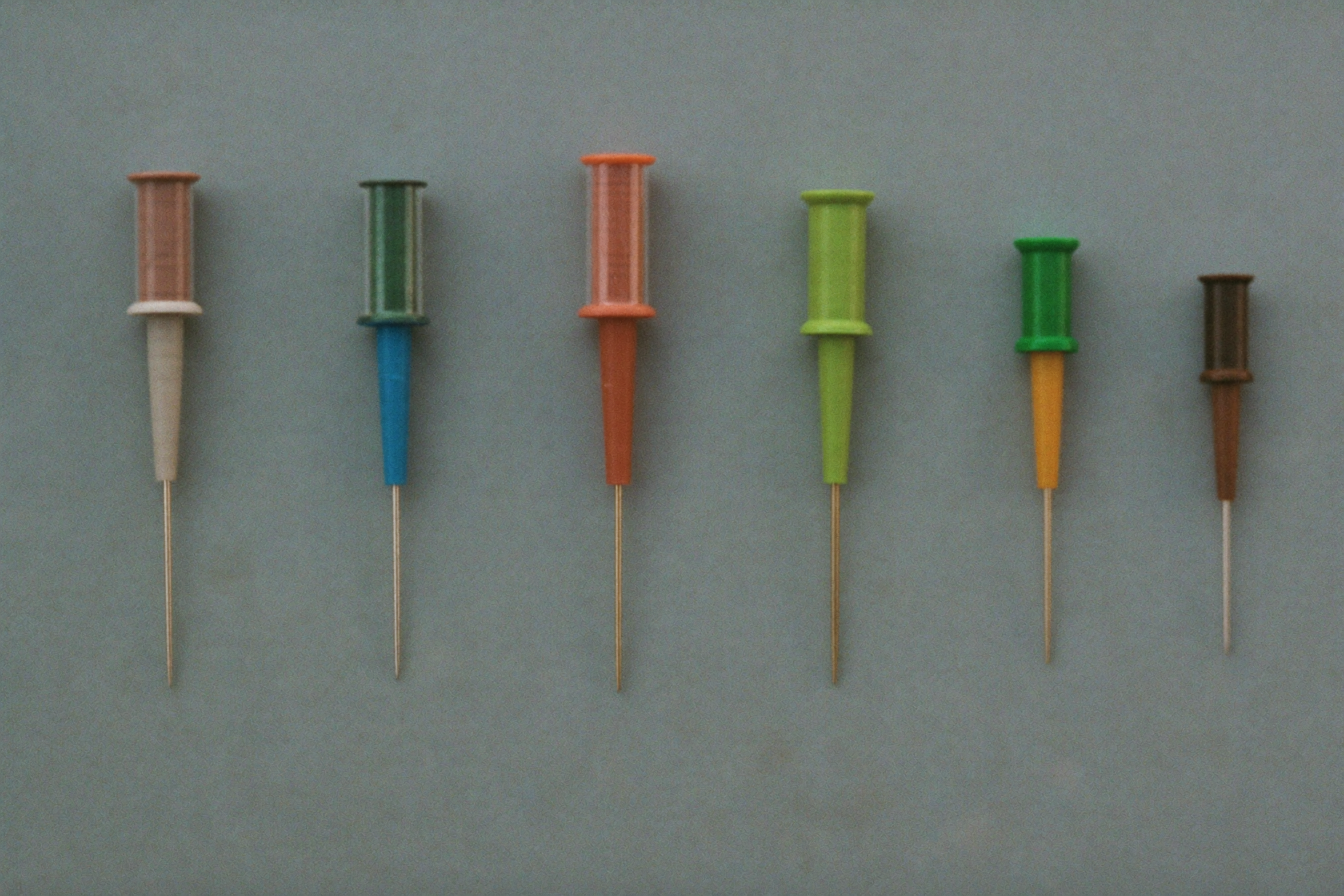 Seven capped needles laid side by side, largest to smallest