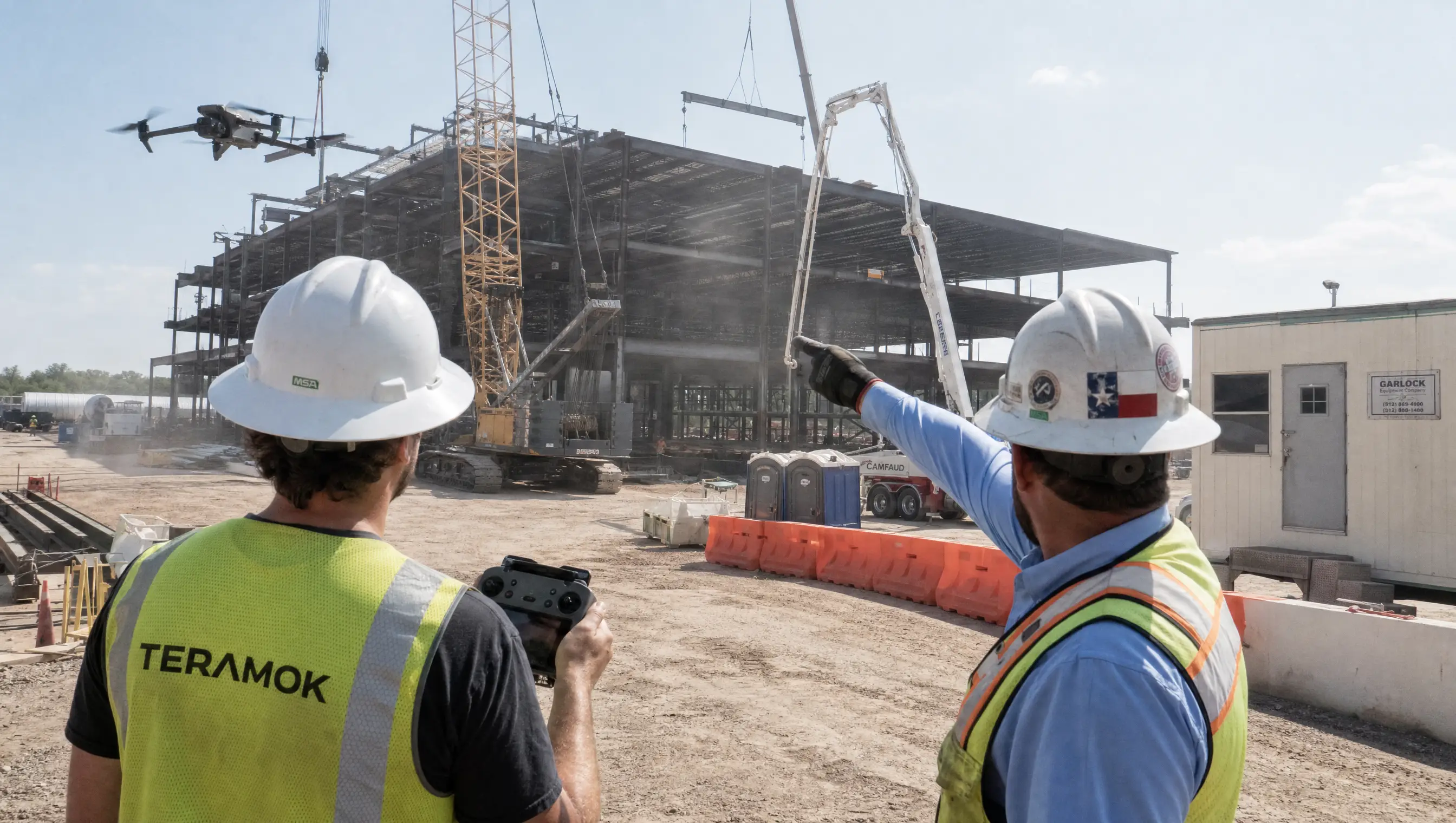 TERAMOK drone pilot in a green safety vest and hard hat flying a drone over a steel-frame building on a Dallas-Fort Worth construction site with the project manager, construction marketing in Dallas
