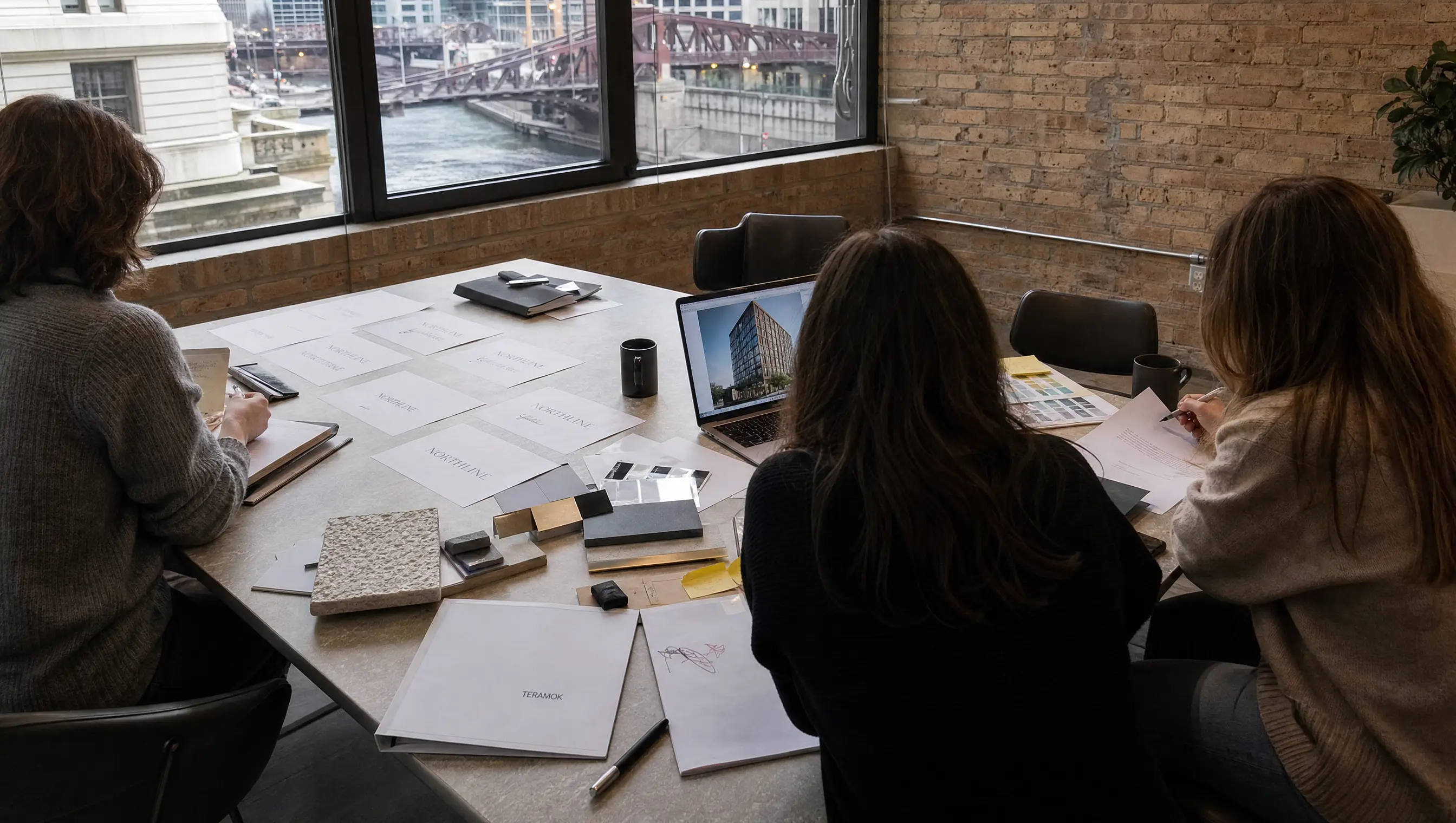 TERAMOK team reviewing building name options, brand books and limestone and bronze samples in a West Loop studio above the Chicago River, real estate branding agency in Chicago