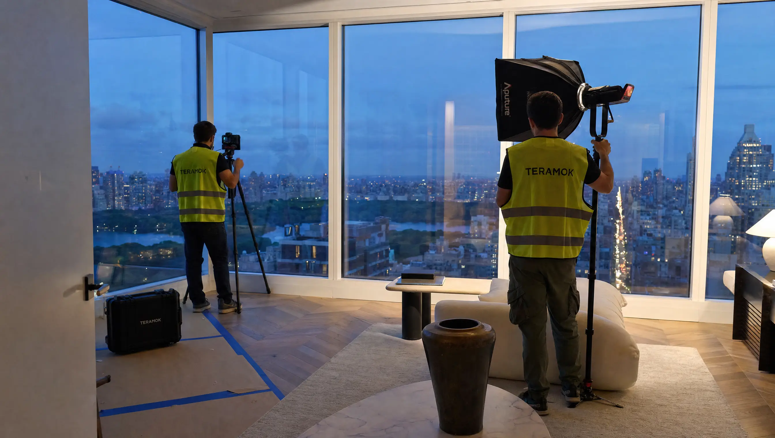 TERAMOK interiors crew in green safety vests setting up a camera and softbox in a Manhattan penthouse overlooking Central Park at dusk, luxury real estate marketing in NYC