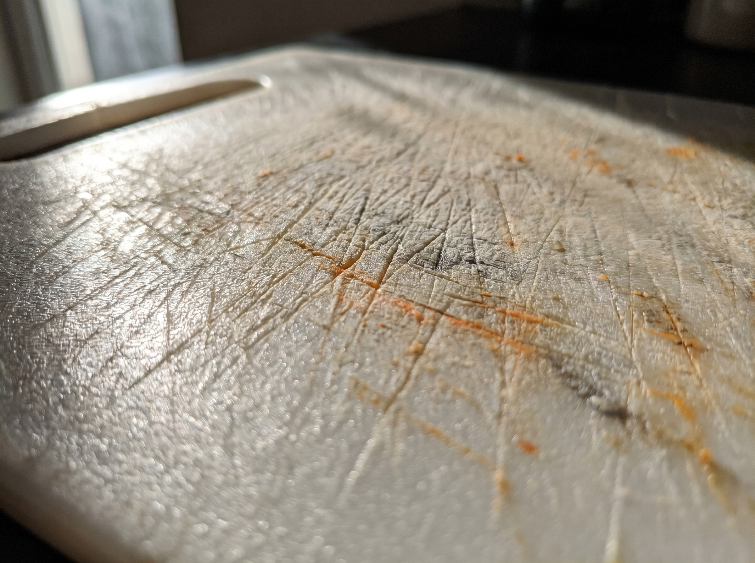 Close-up of deep grimy knife grooves in a worn plastic chopping board