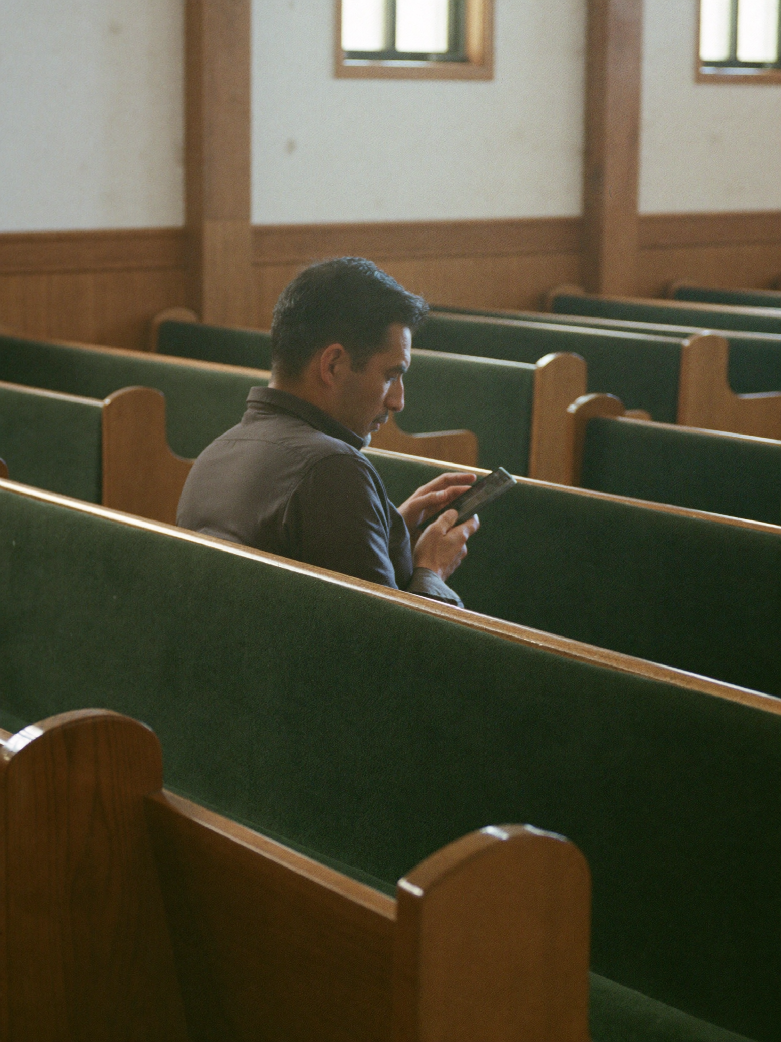 A pastor sitting alone in an empty pew, reading his phone