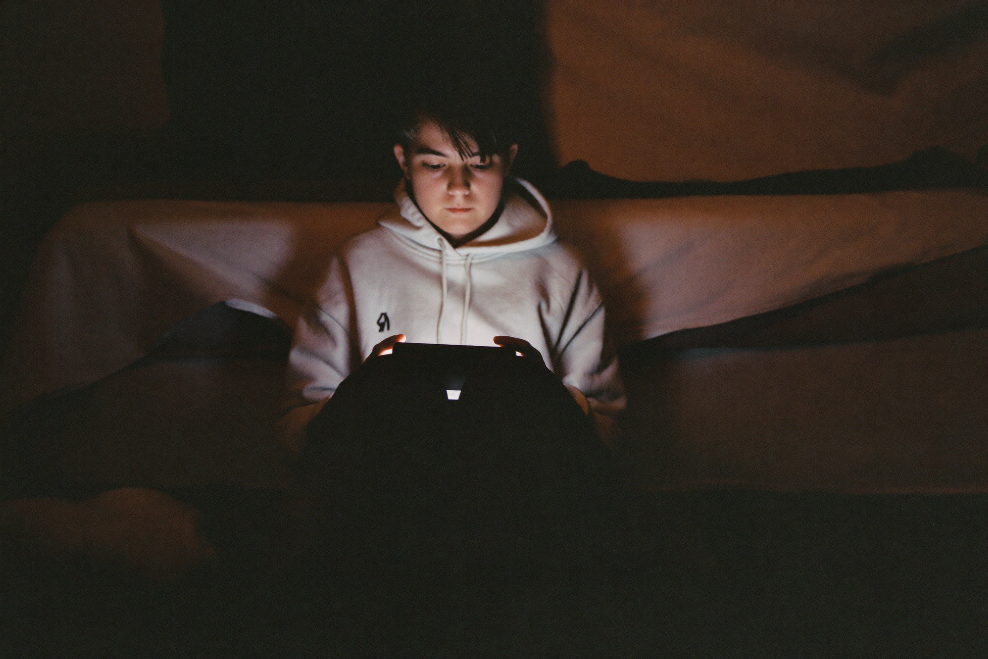 A teenager in a dark room, face lit by a screen