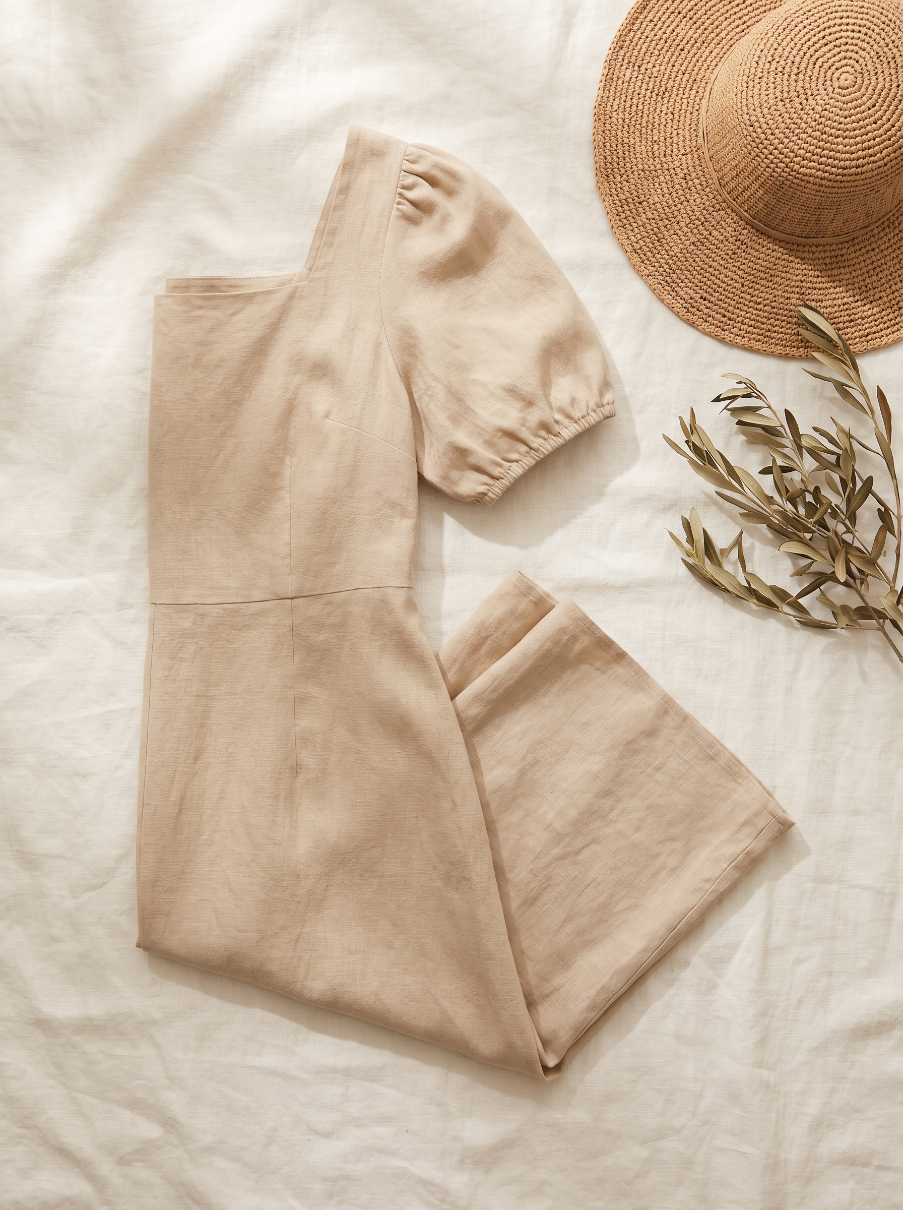 A folded sand-coloured summer dress styled with a sun hat