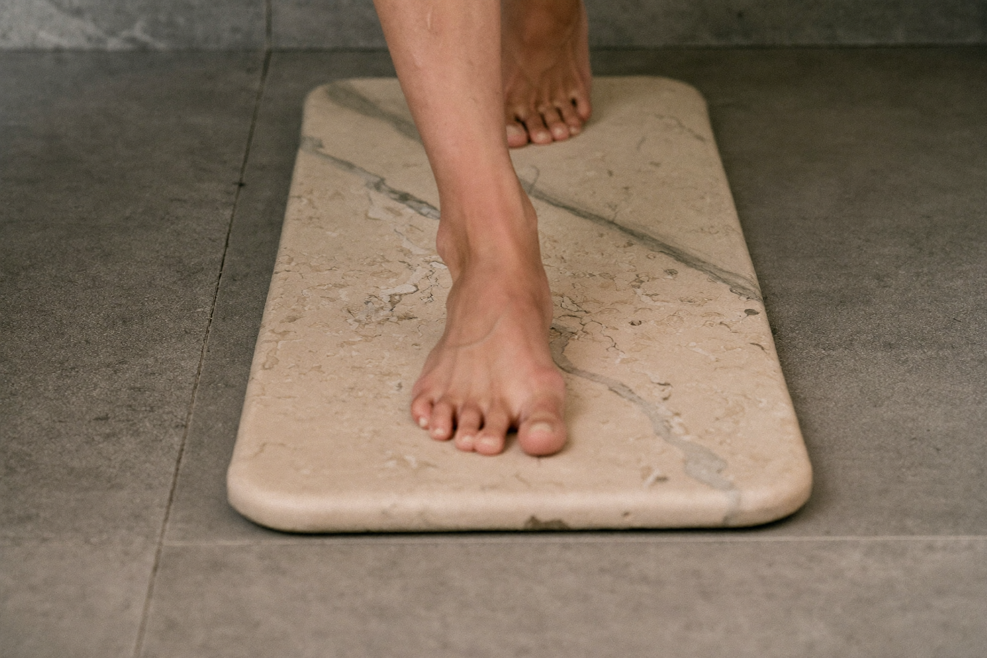 Close-up of bare feet stepping onto a textured bath mat in a minimal bathroom