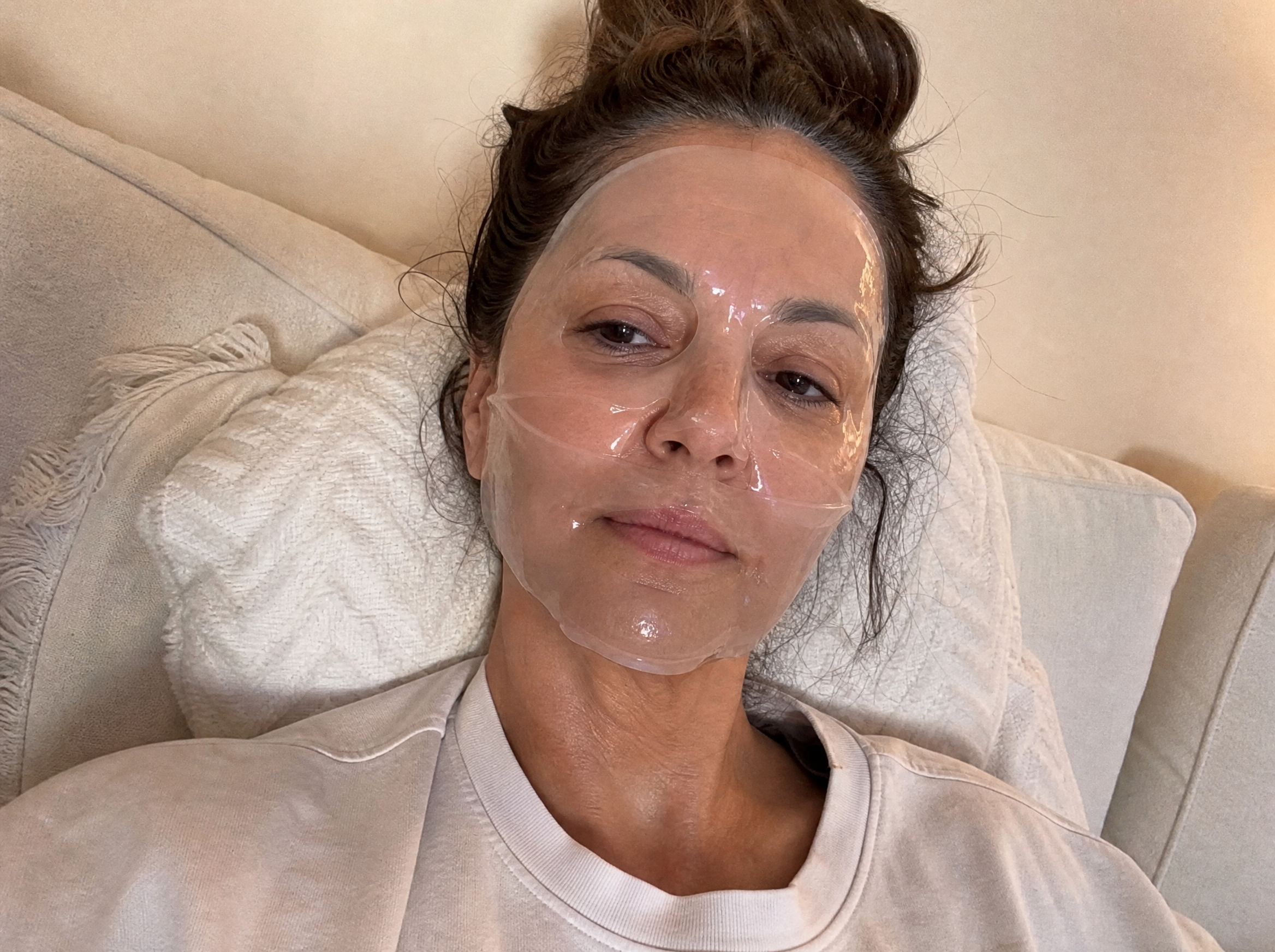Woman reclining on a couch with a clear collagen hydrogel mask molded to her face like a second skin