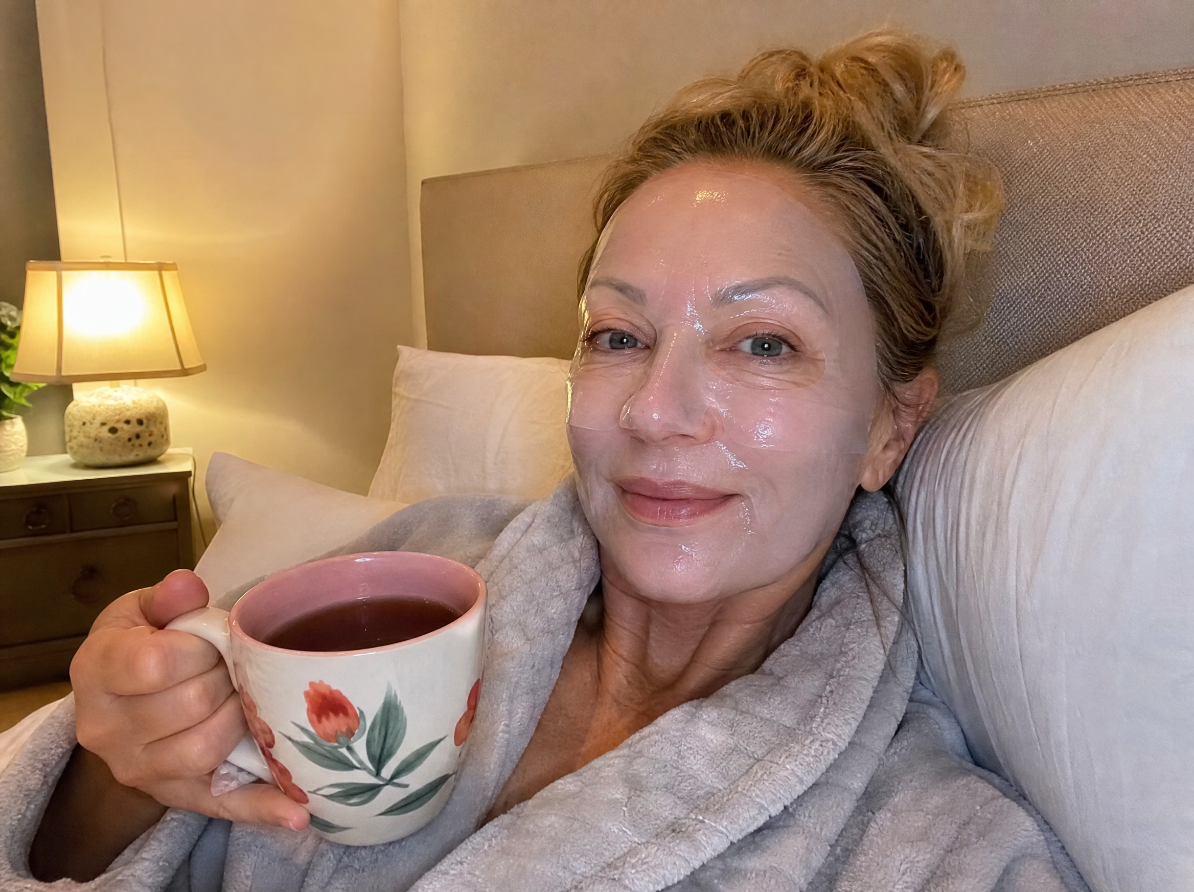Woman relaxing in the evening with a clear collagen mask on, cup of tea, glowing skin