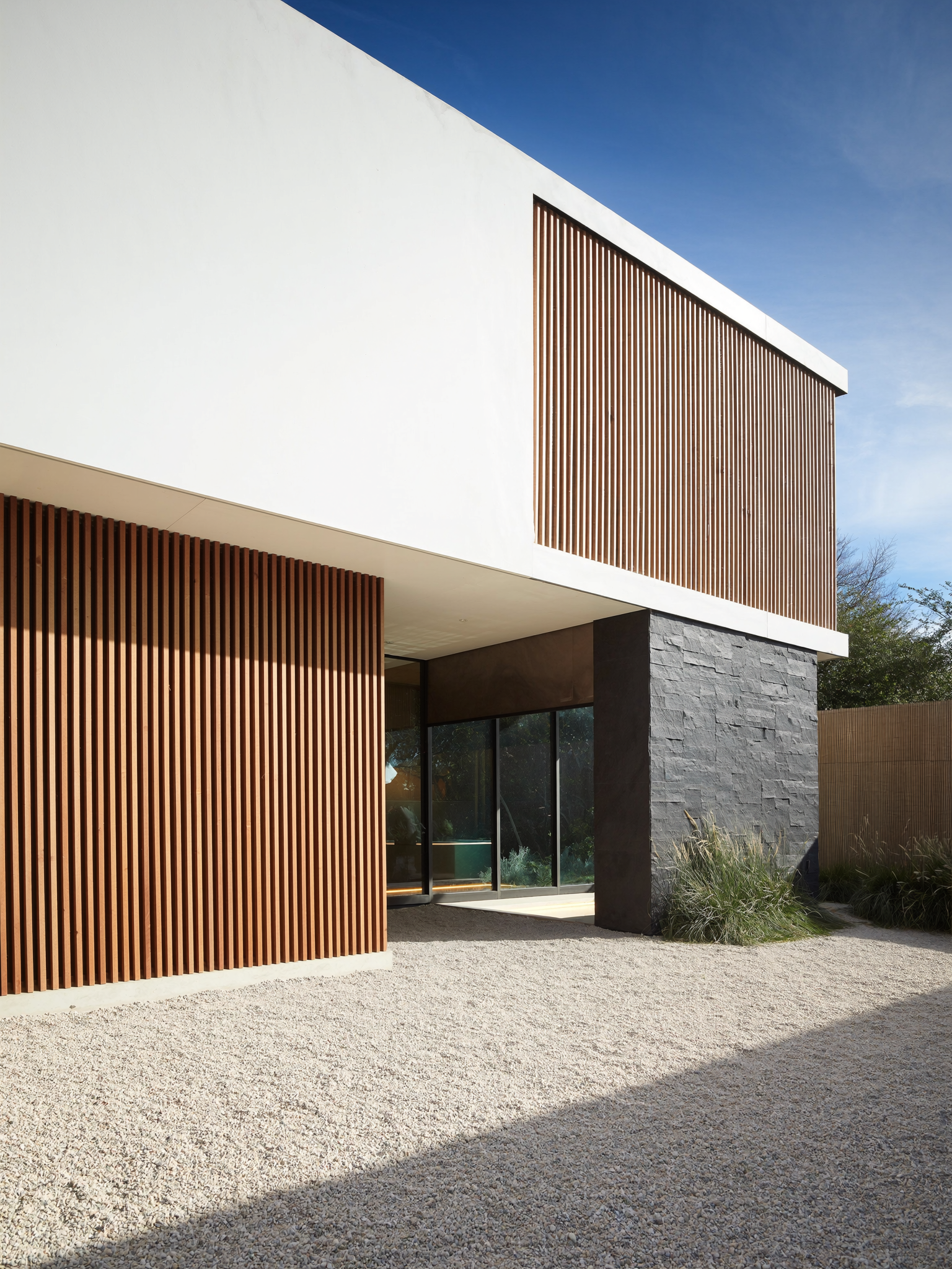 Vivienda de dos plantas con fachada blanca y celosía de madera vertical