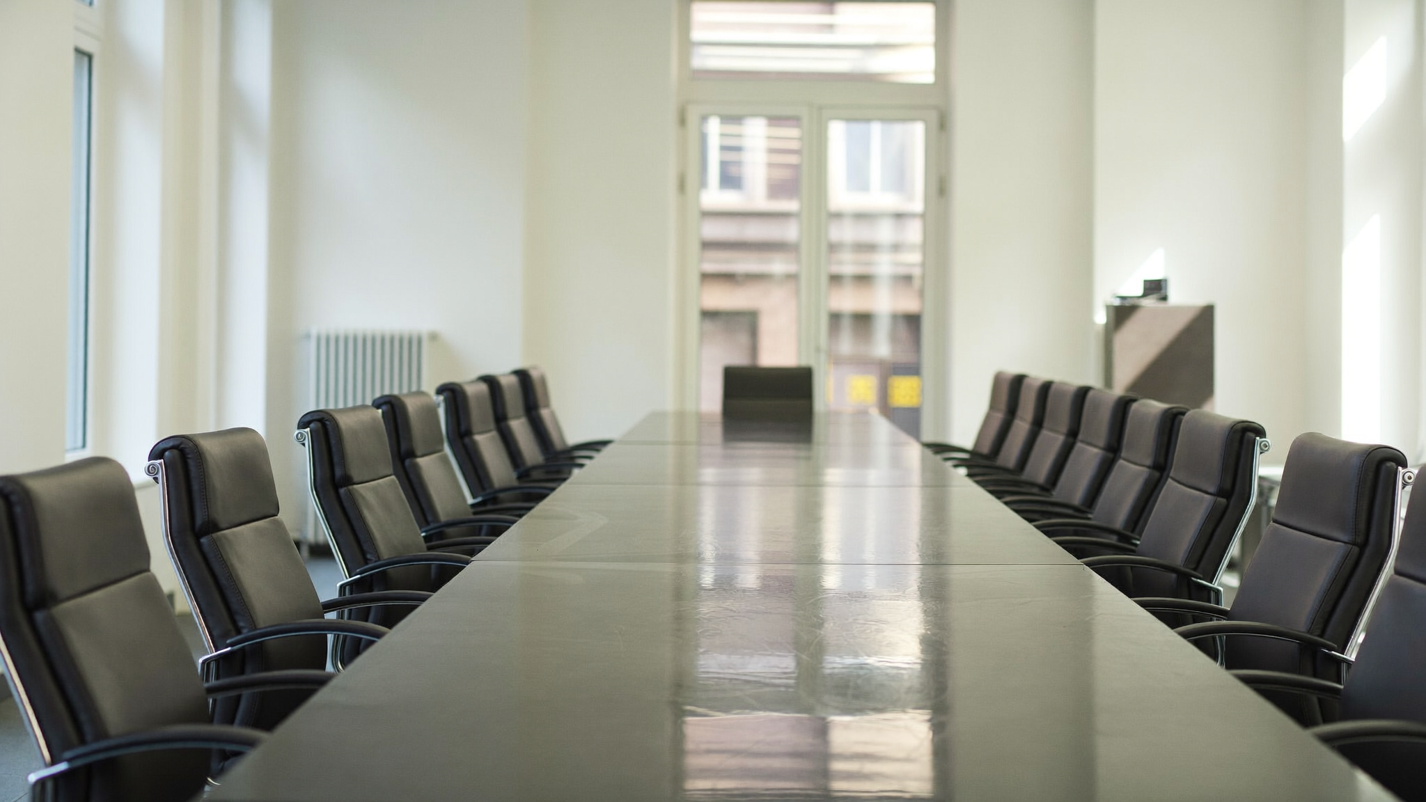 Leerer Sitzungssaal mit langem Konferenztisch und unbesetzten Stühlen