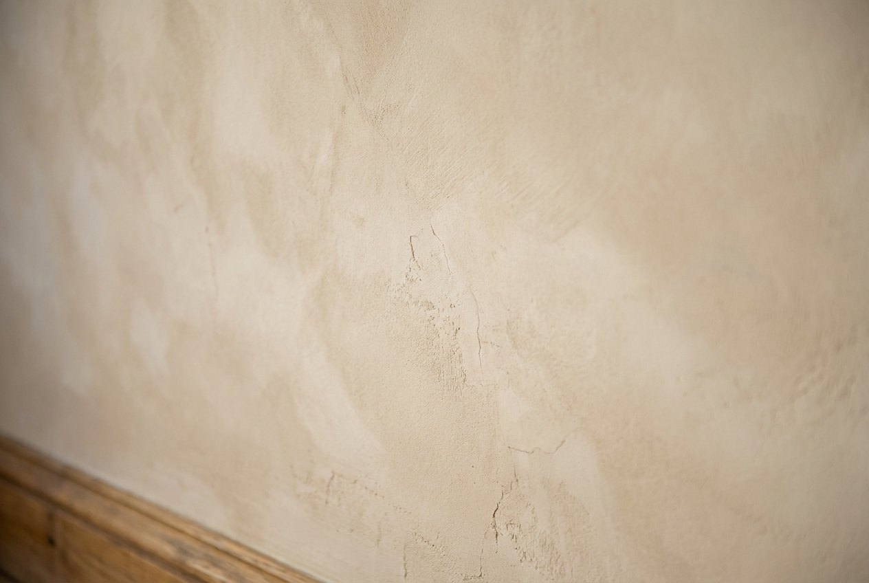 Close-up of a lime-washed interior wall showing soft chalky matte texture and warm oak skirting