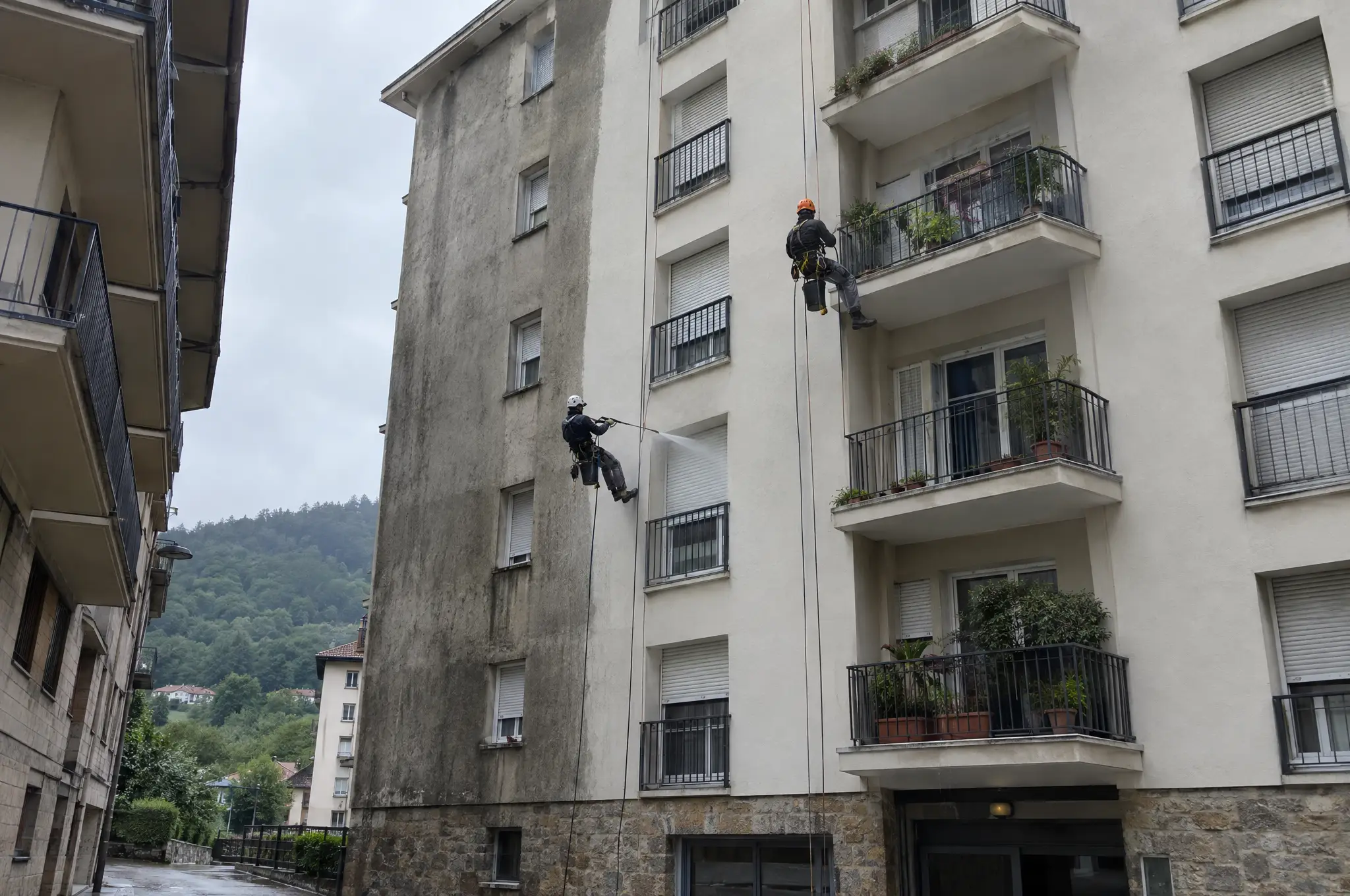 Dos técnicos en cuerda limpiando con agua a presión la fachada de un edificio de viviendas