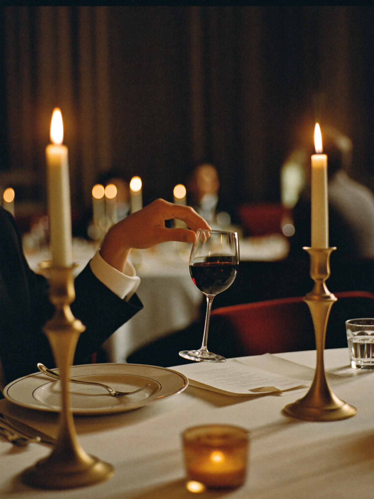 A professional swirling a glass of red wine at a candlelit business dinner