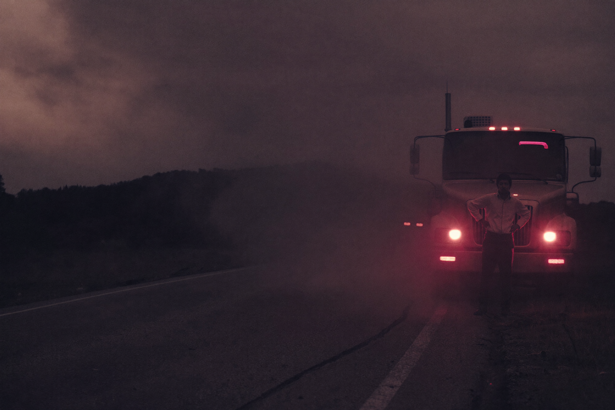 An HVAC technician standing beside his truck on an empty road at dusk