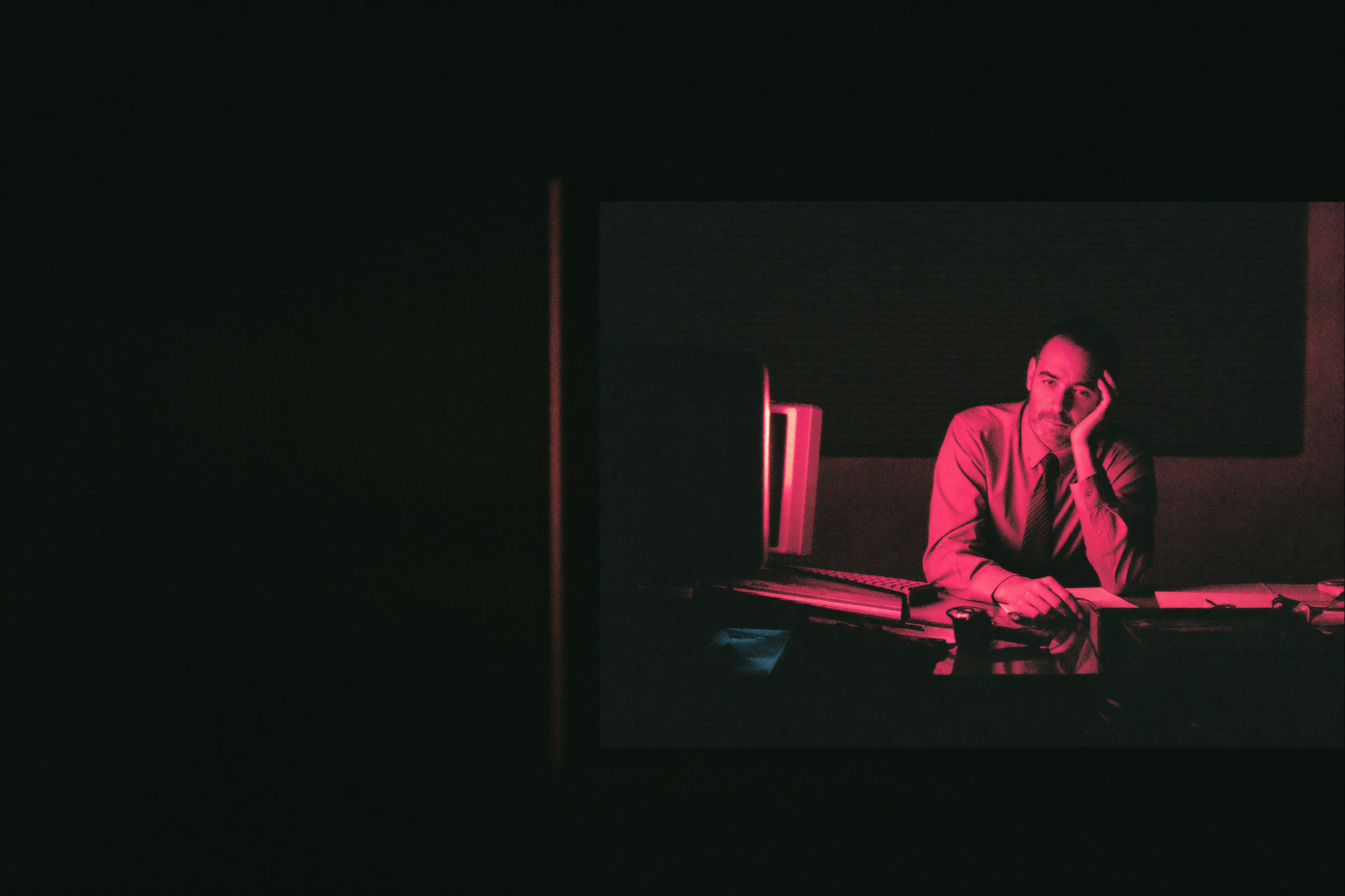 A trades business owner alone at a cluttered desk late at night with a stack of paperwork