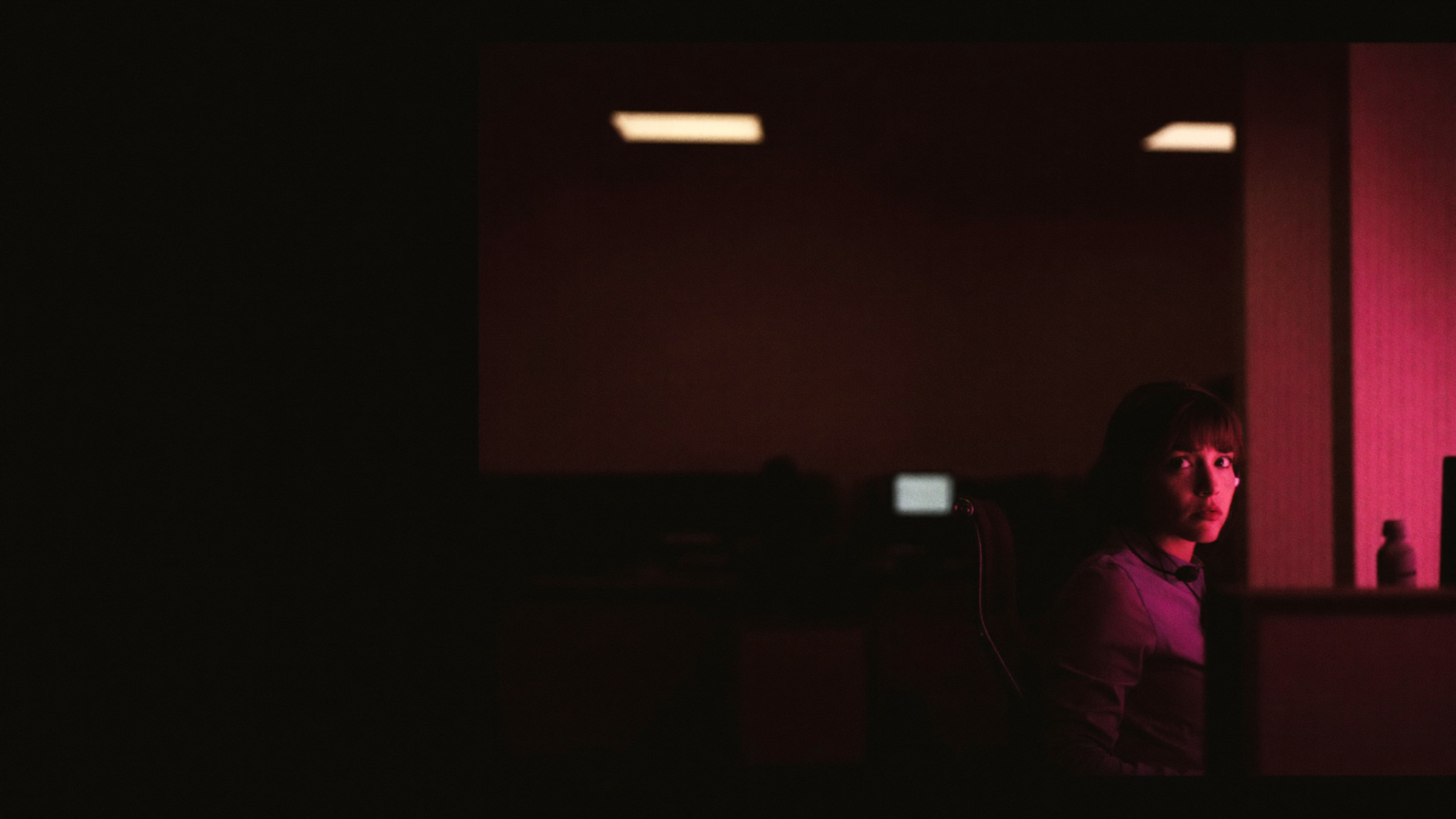 A dispatcher wearing a headset in a dim office, lit in magenta