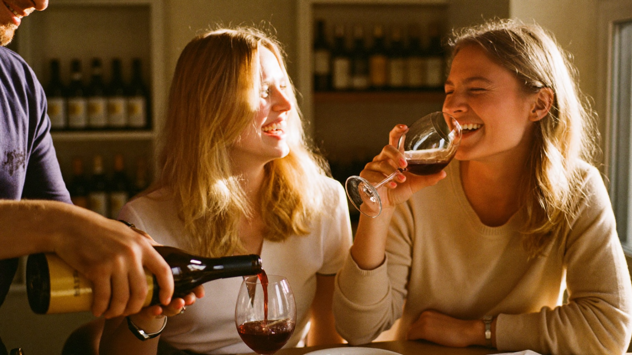 Friends laughing over a glass of wine with a sommelier at a warm wine bar