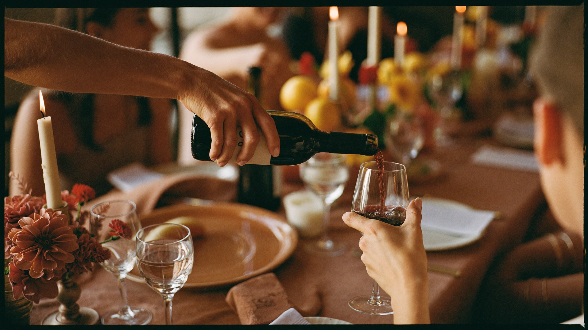 Red wine being poured at a warmly set golden-lit dinner table
