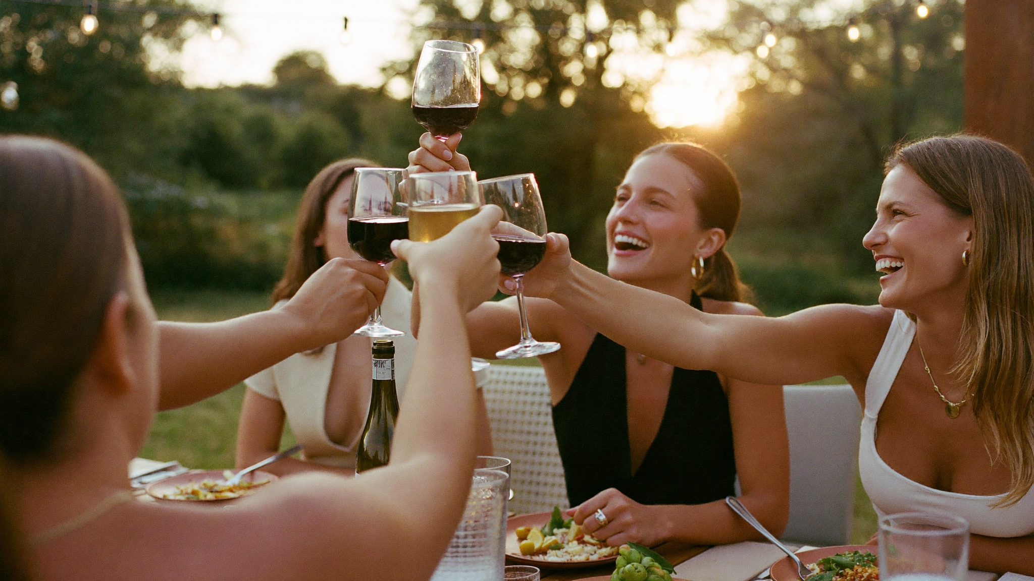 Group of friends clinking wine glasses around a table at sunset