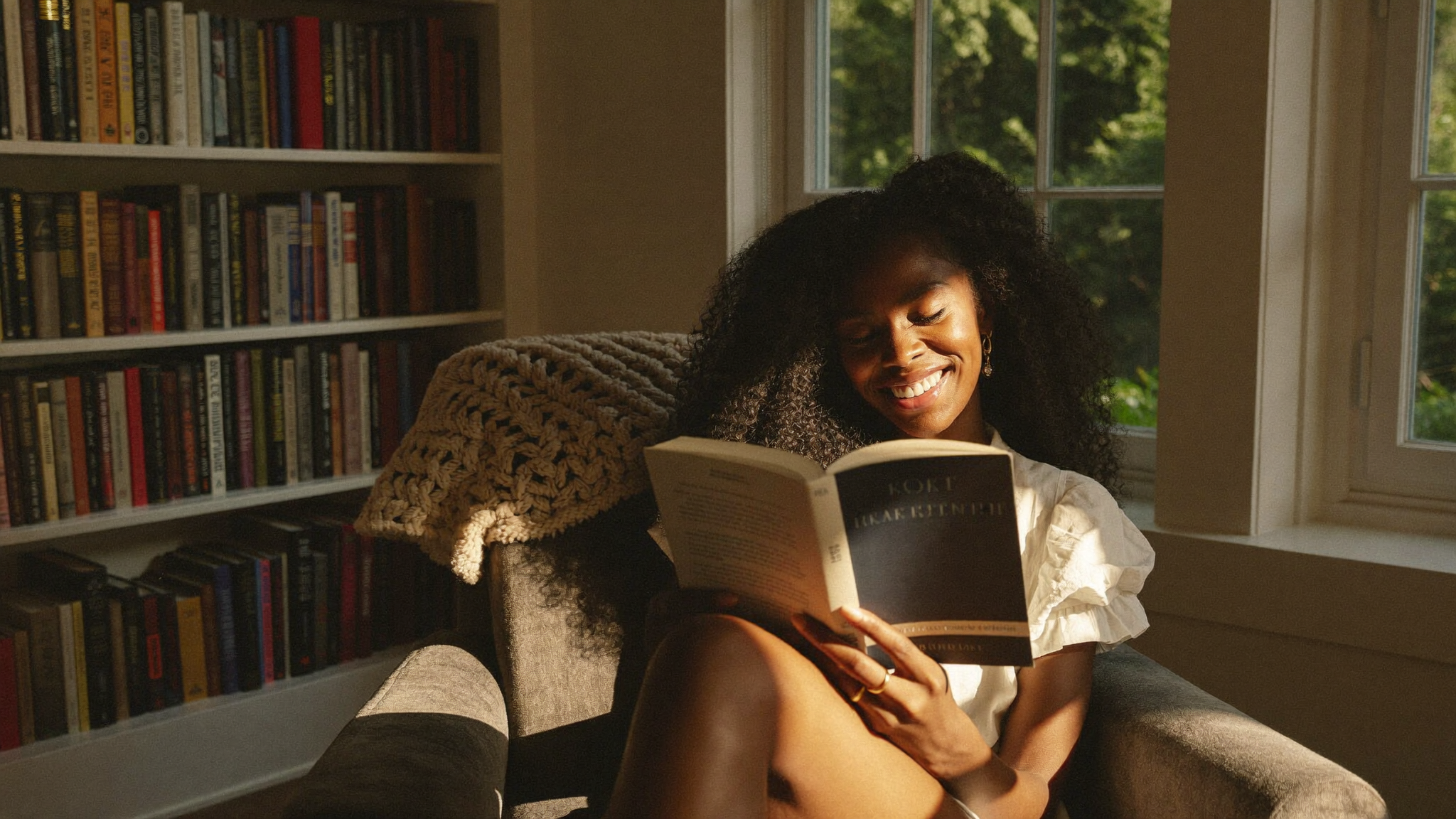 Black woman reading in a cozy armchair with warm afternoon light