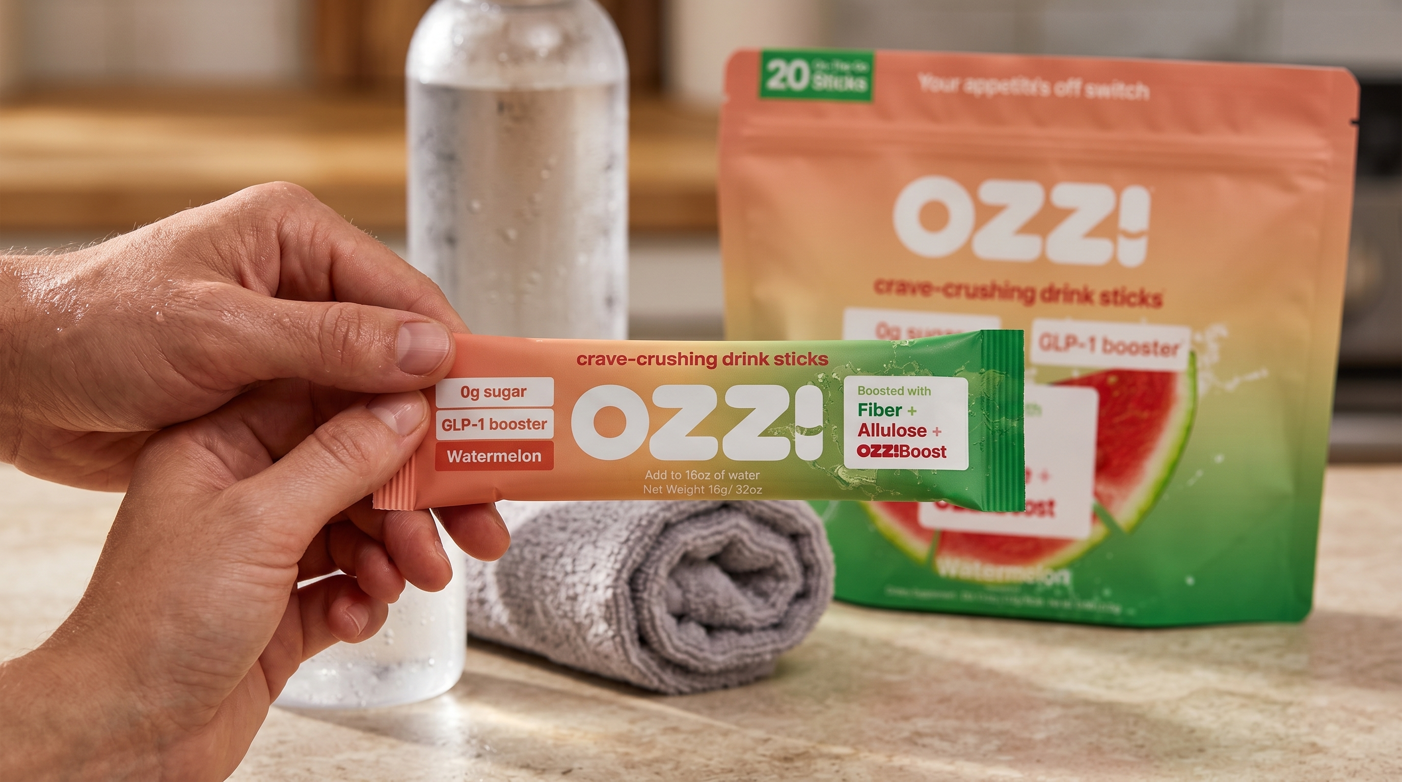 A hand holding a single OZZ! watermelon stick pack after a home workout with a towel and water bottle nearby