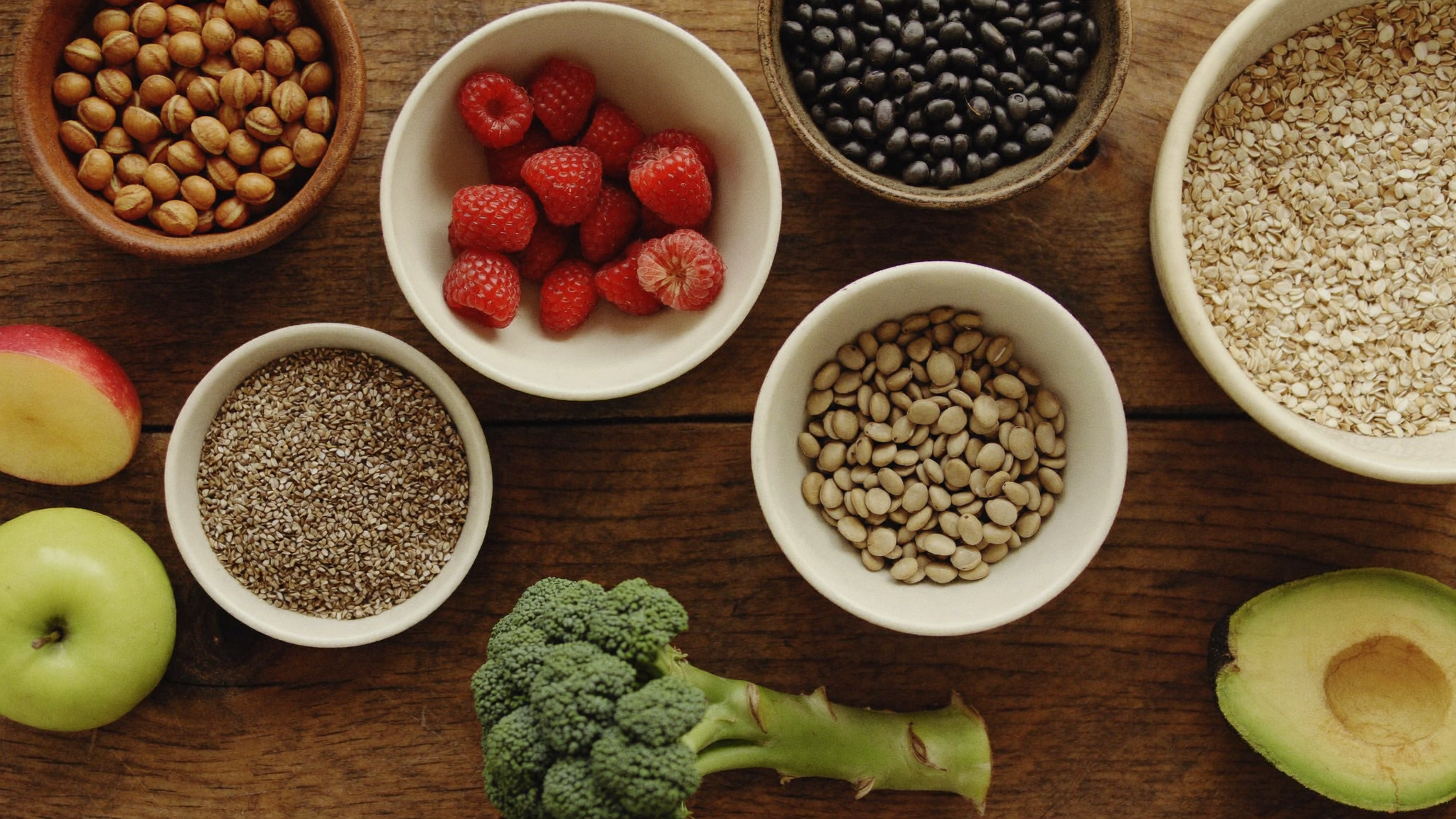An overhead flatlay of high-fiber whole foods including oats, chia, beans, lentils, berries, and vegetables