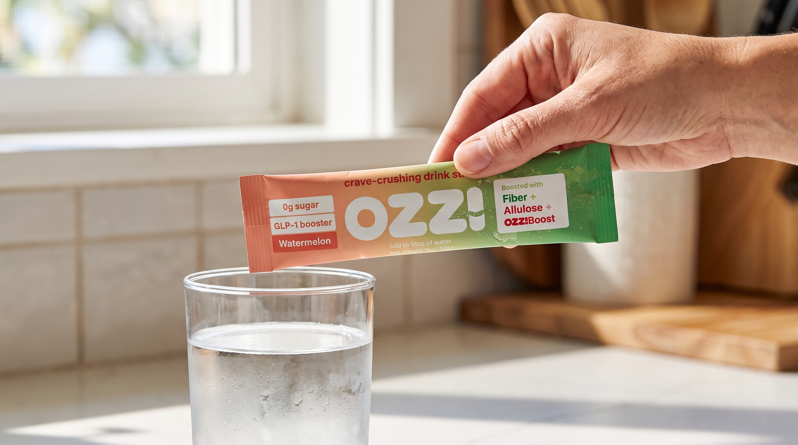 Close-up of a hand holding a single Ozzi watermelon stick pack above a glass of cold water