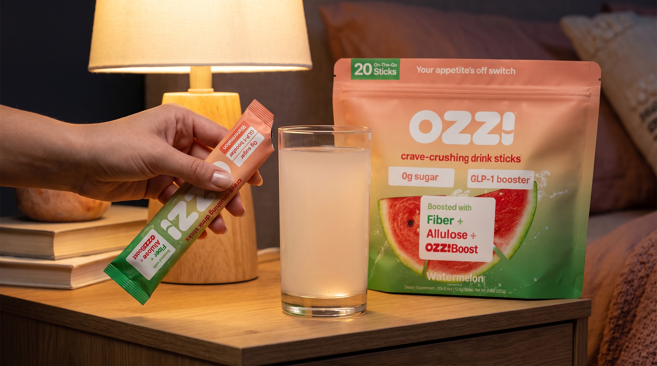 Hand tearing open an Ozzi watermelon stick pack next to a glass of the prepared drink on a nightstand