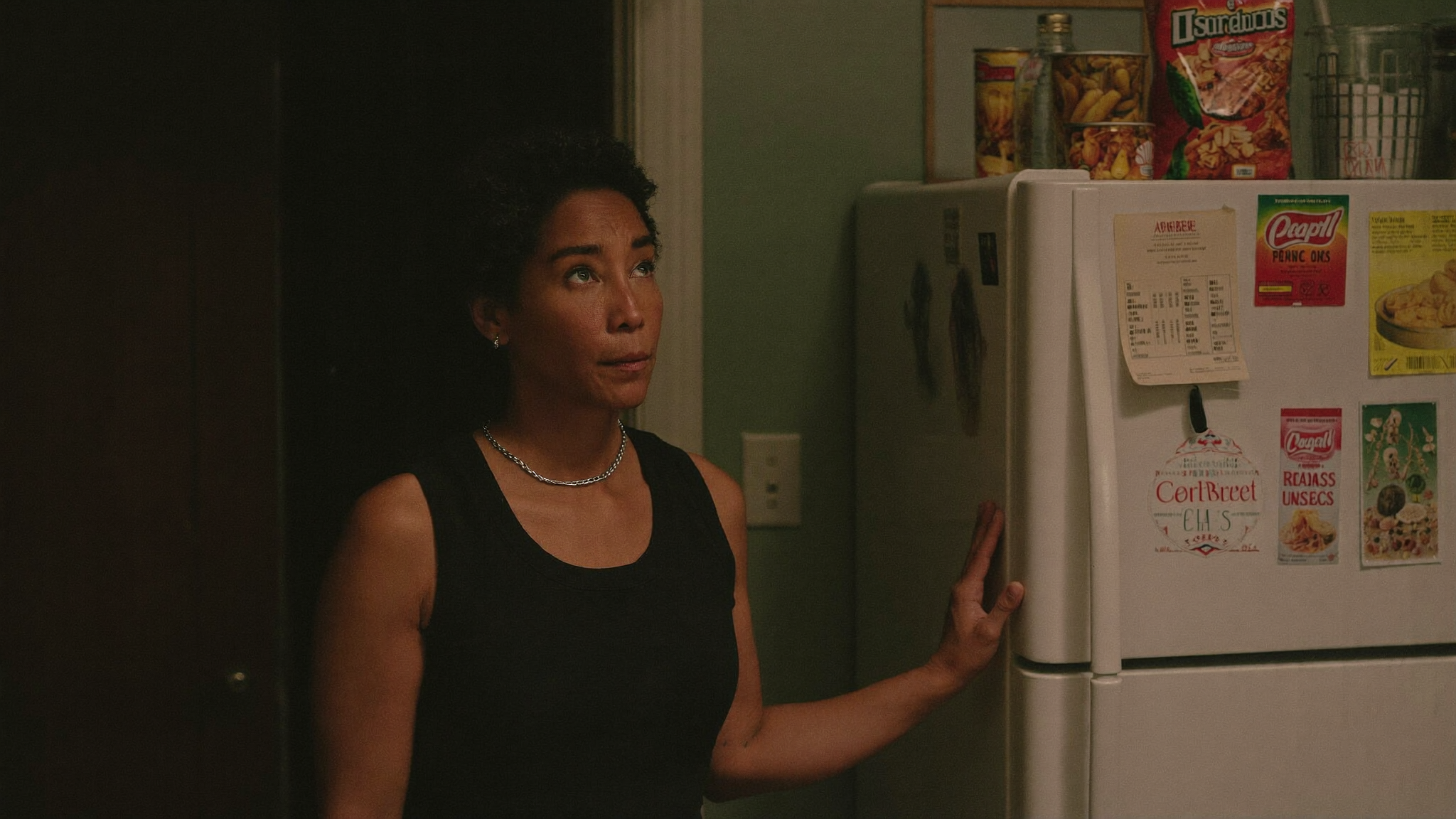 A woman standing calmly in a dim kitchen at night near a closed snack cabinet
