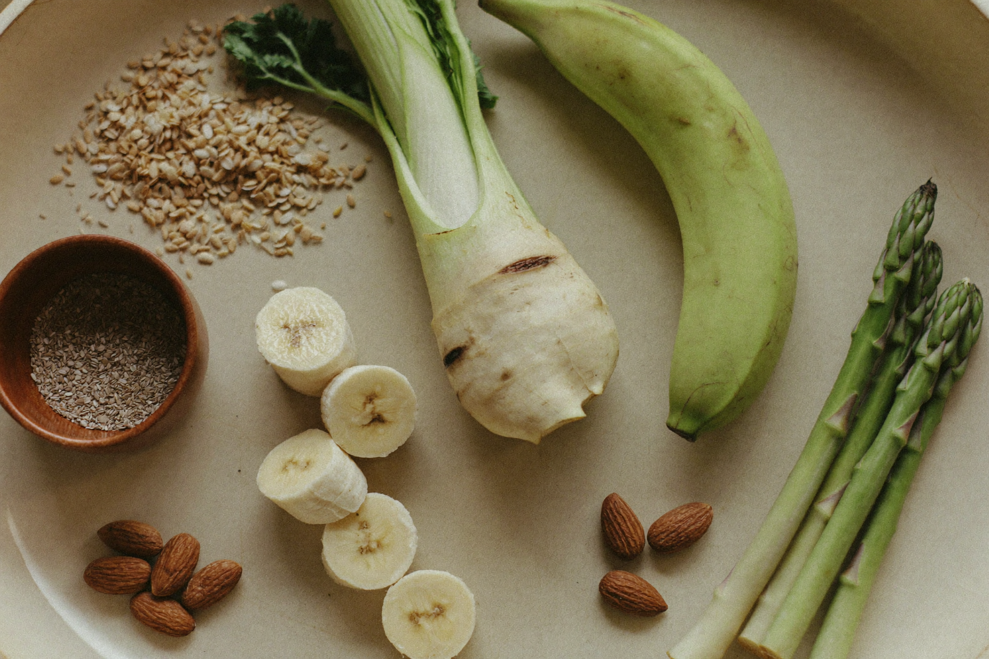 Overhead flat lay of whole food fiber sources including chicory root, oats, green banana, almonds and flaxseed