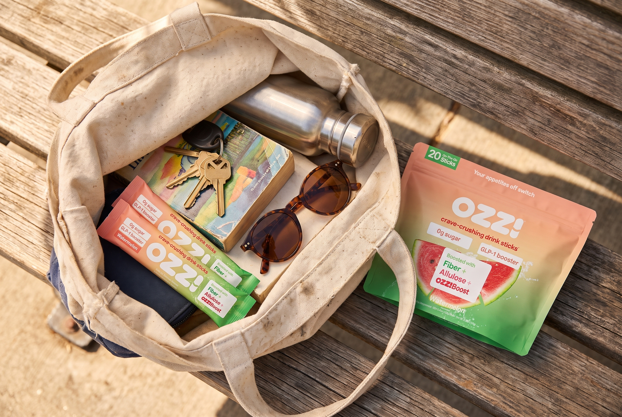 An open canvas tote bag containing keys, a book, a water bottle and two Ozzi stick packs