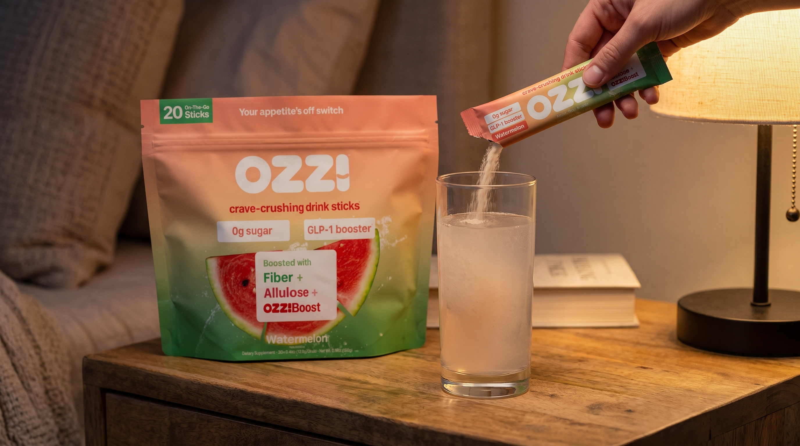 A hand pouring an Ozzi watermelon stick pack into a glass of water on a nightstand at night, next to the Ozzi pouch.