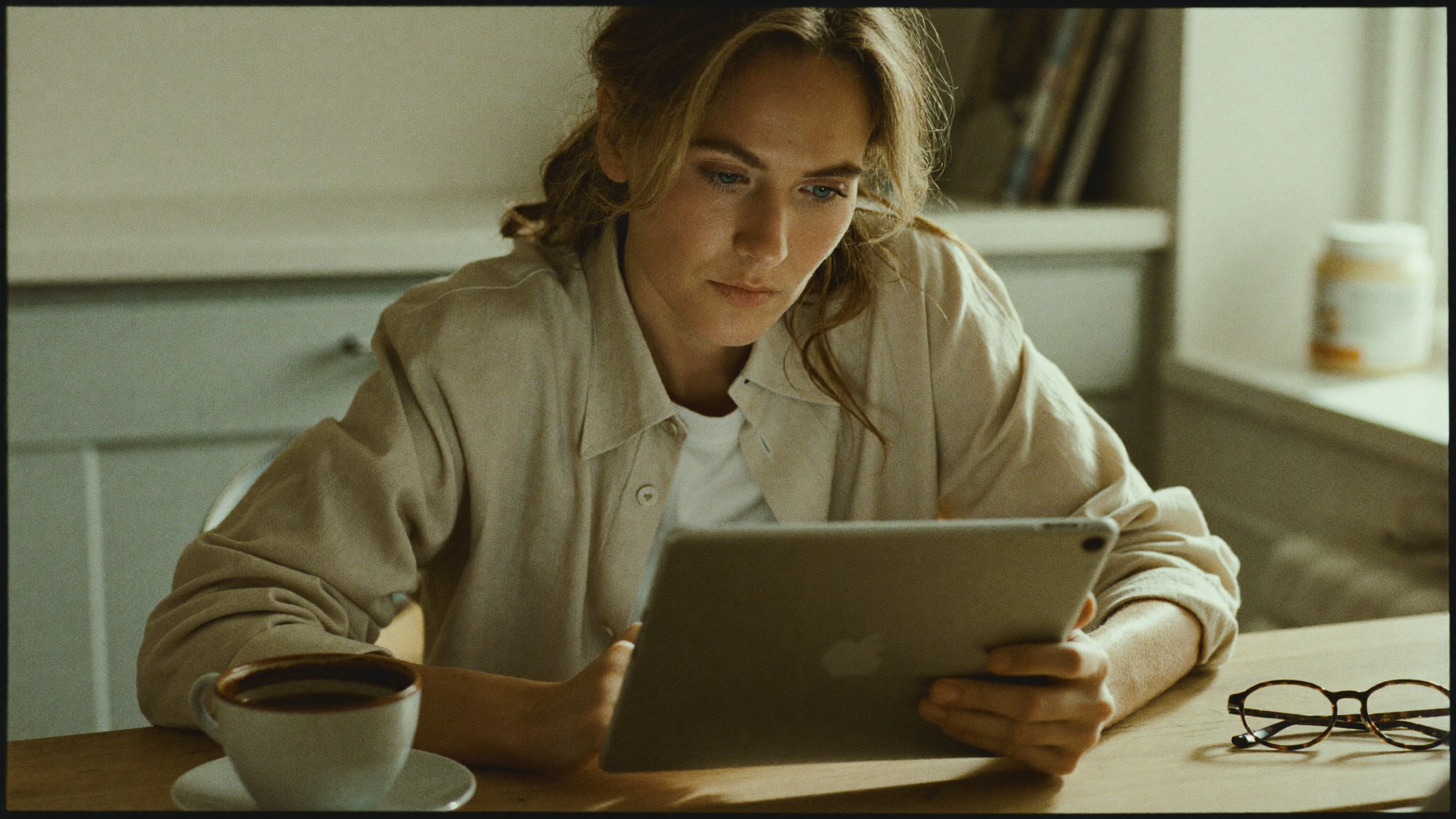Woman in her forties reading nutrition research on a tablet at a kitchen table in warm morning light