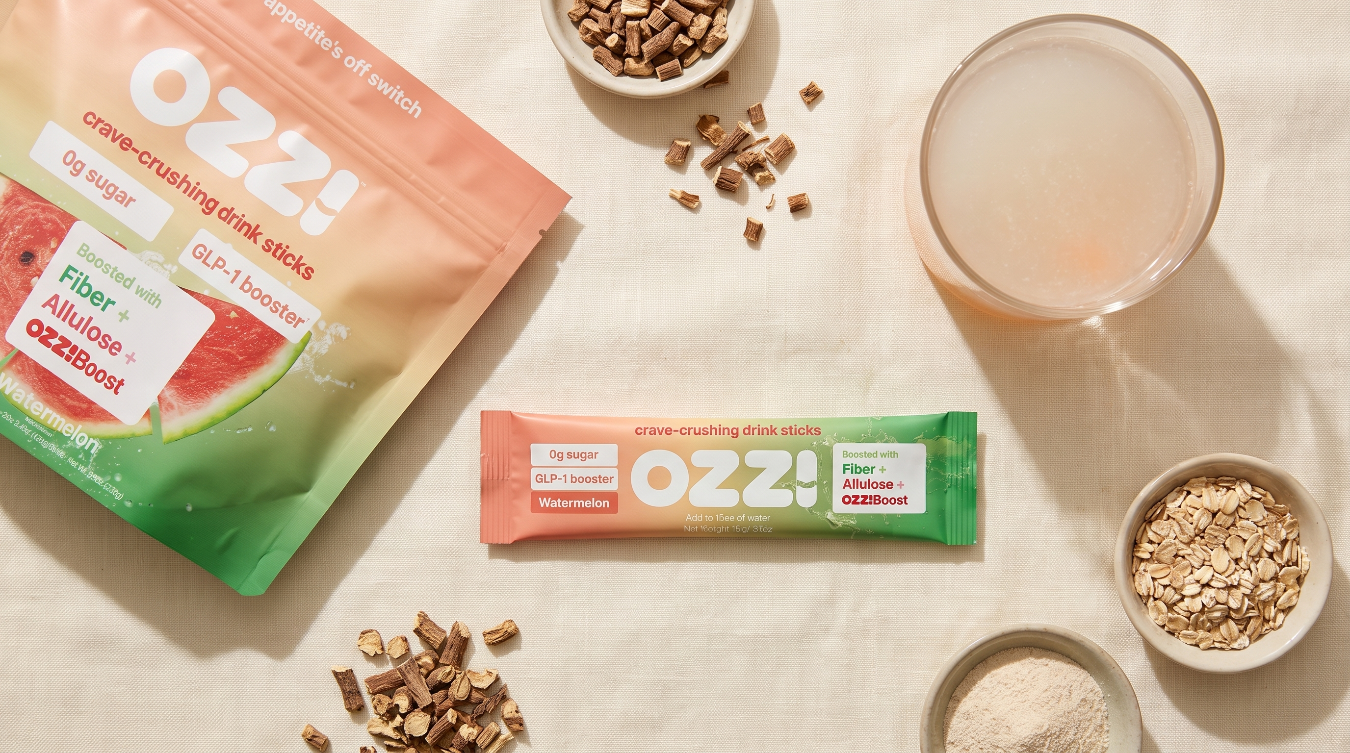Ozzi watermelon stick pack pouch and single stick on a kitchen counter beside a prepared glass of the drink