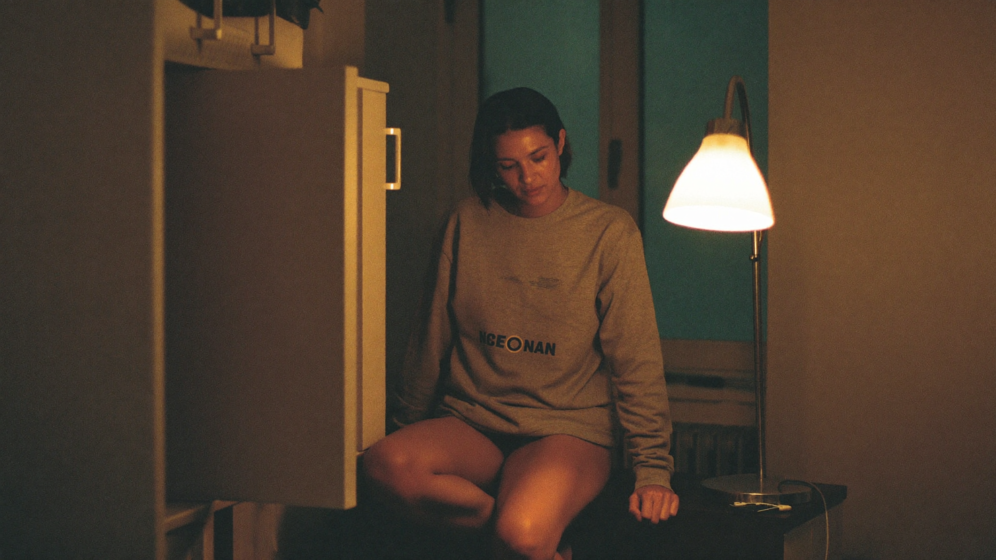 A woman sitting alone in a dim kitchen late at night, looking tired