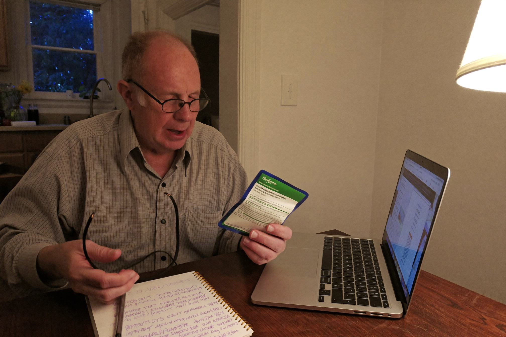 An older man reading a supplement label at his kitchen table