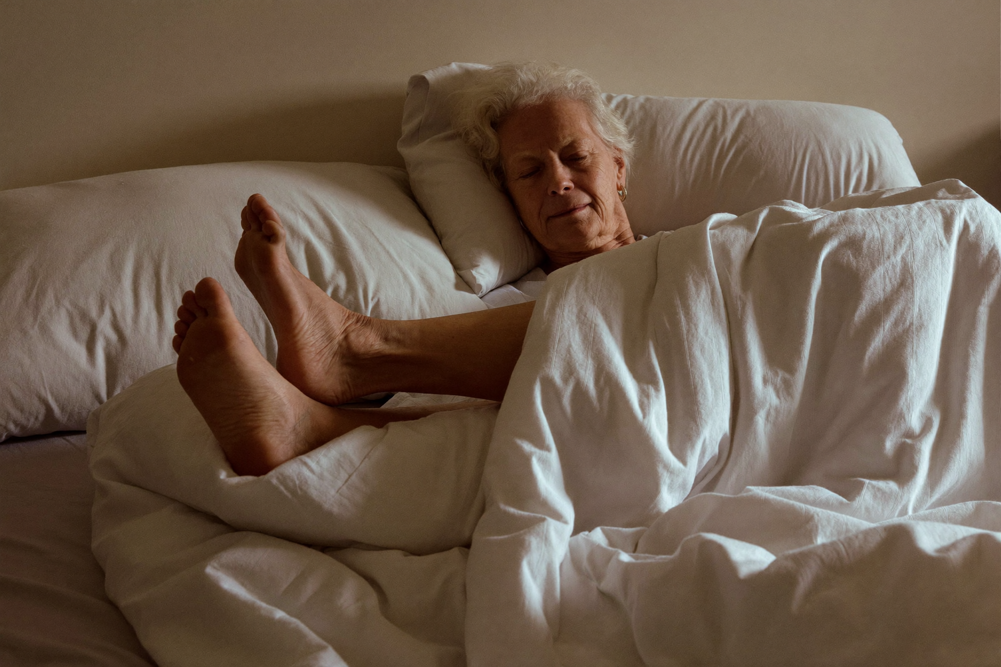 An older woman waking calmly with her feet under the covers in morning light