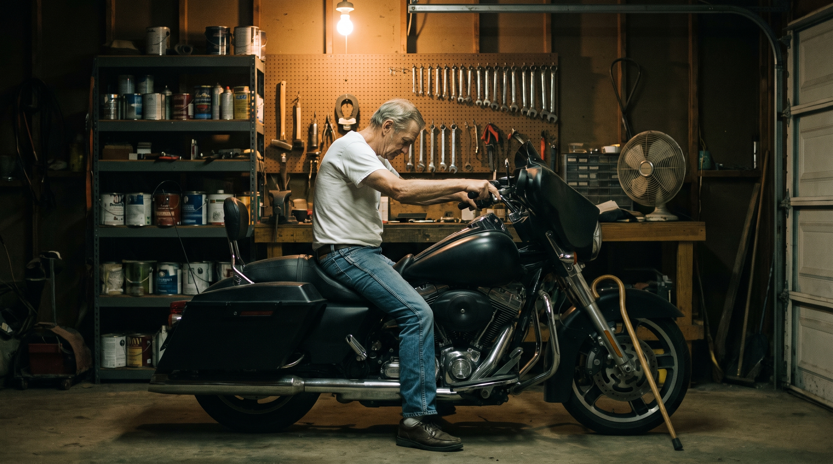 A 73 year old rider sitting on his motorcycle in a dark garage at four in the morning, a cane leaning against the front wheel