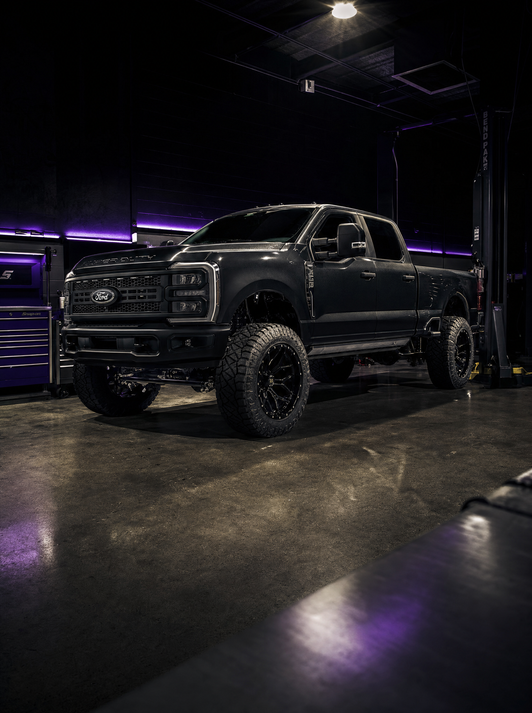 Modified Ford F-250 Super Duty inside a dark professional shop with purple LED lighting
