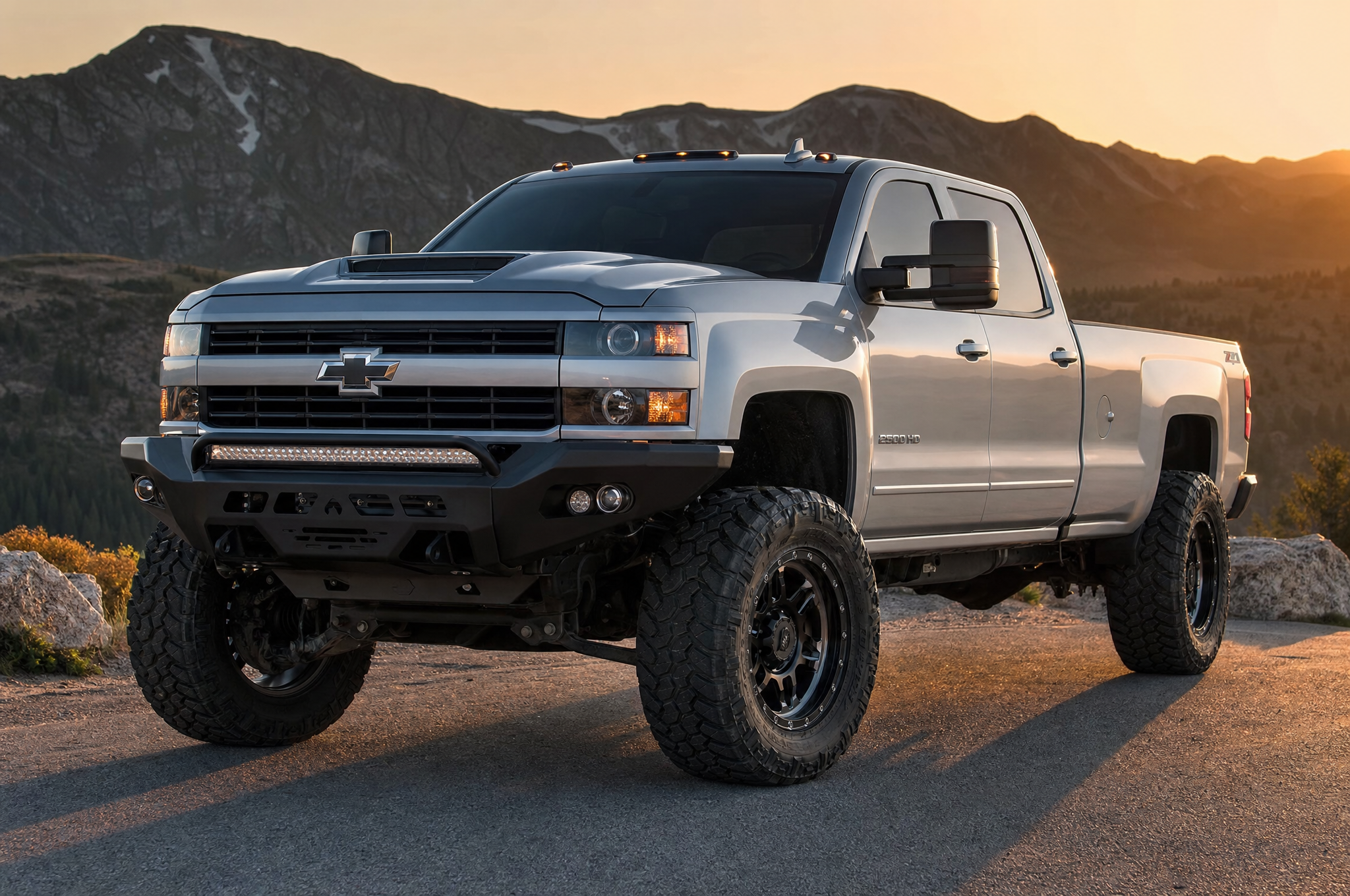 Modified silver Chevy Silverado 2500HD with lift kit and off-road tires on a mountain road