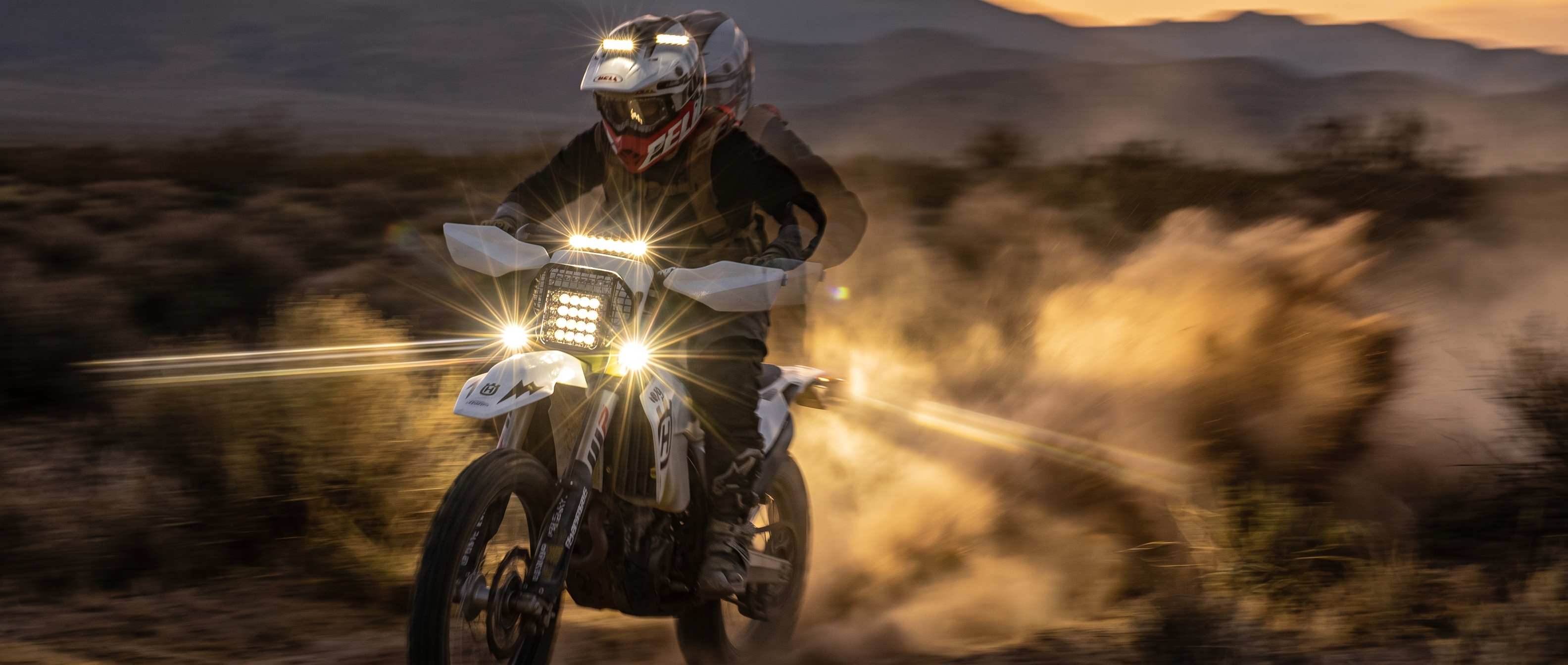 Dirt bike rider running a high-output LED headlight at golden hour