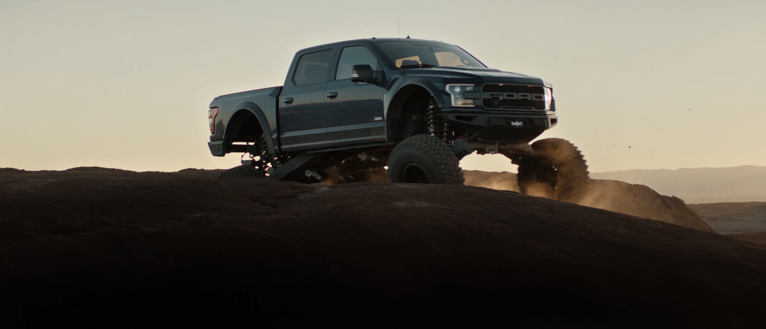 Lifted Ford F-150 Raptor articulating over desert rock