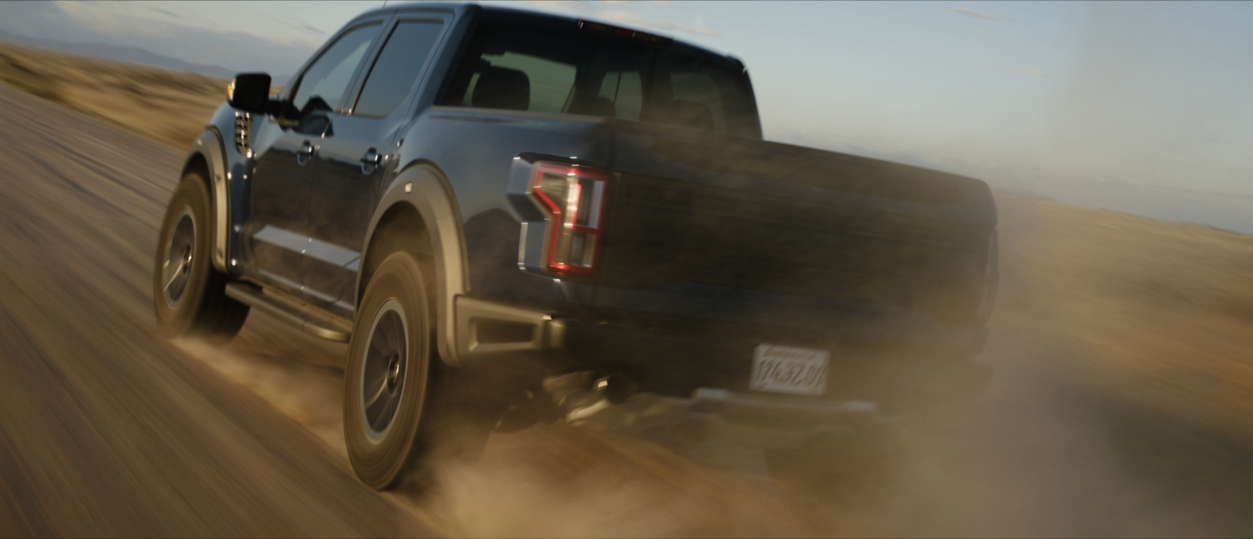 Ford Raptor blasting through high desert with dust trail