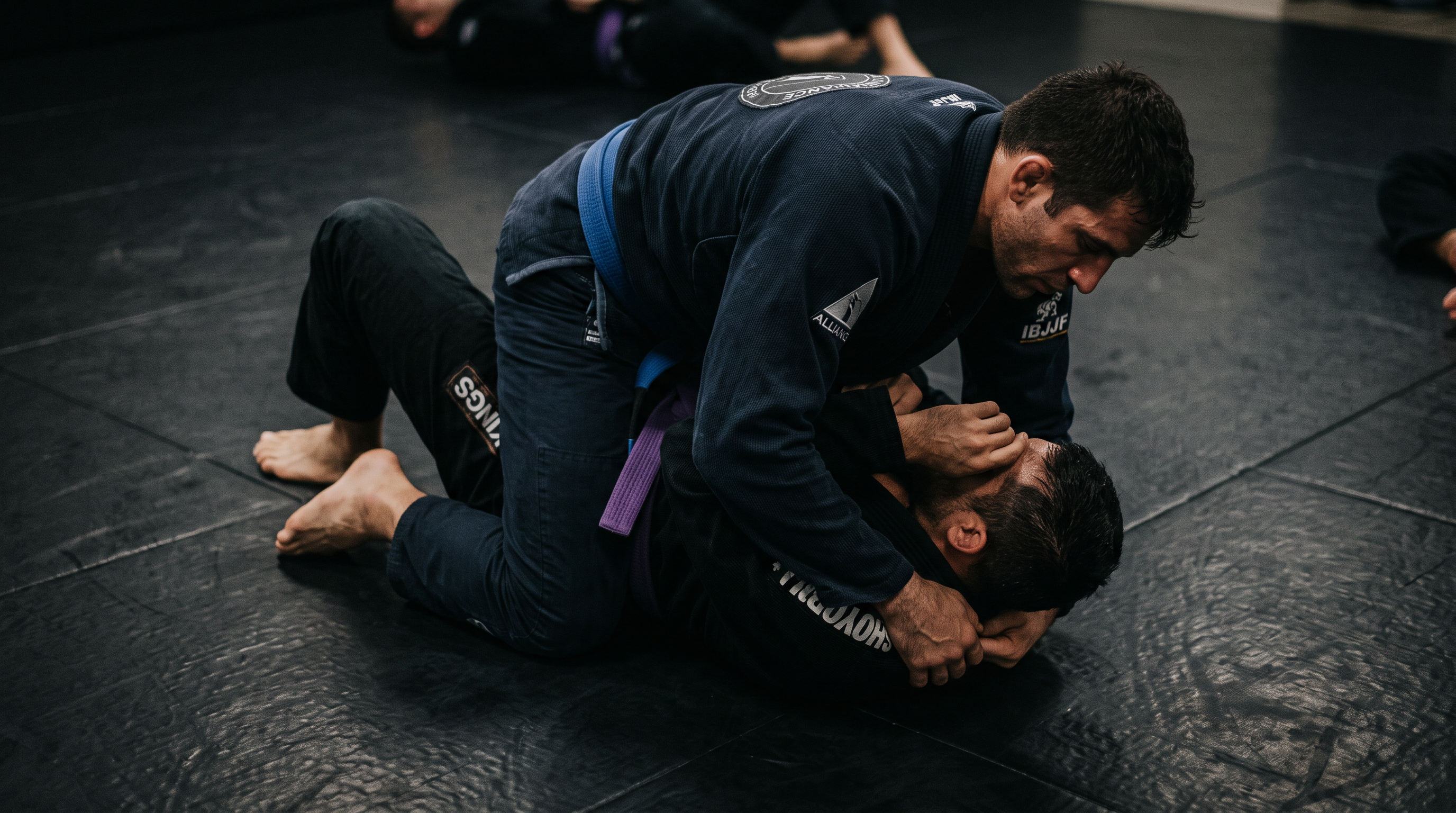 Two BJJ practitioners in dark gis demonstrating the north-south pin position on a black training mat.