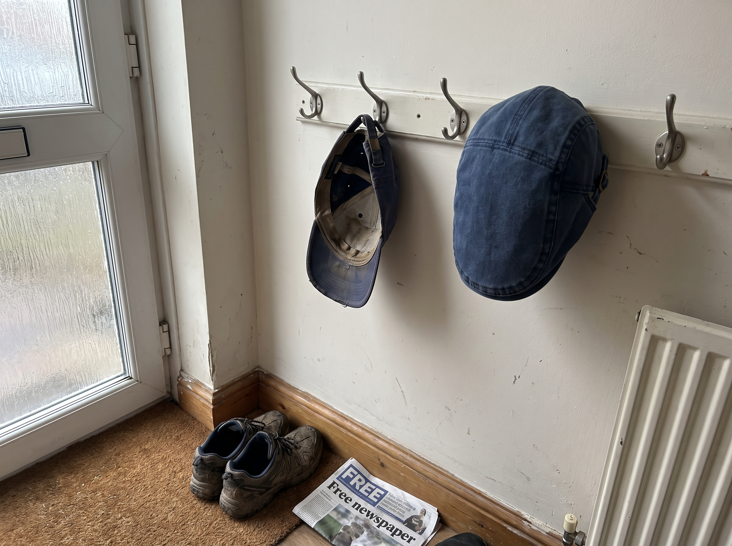 An old faded baseball cap hanging beside the new denim flat cap on hallway hooks