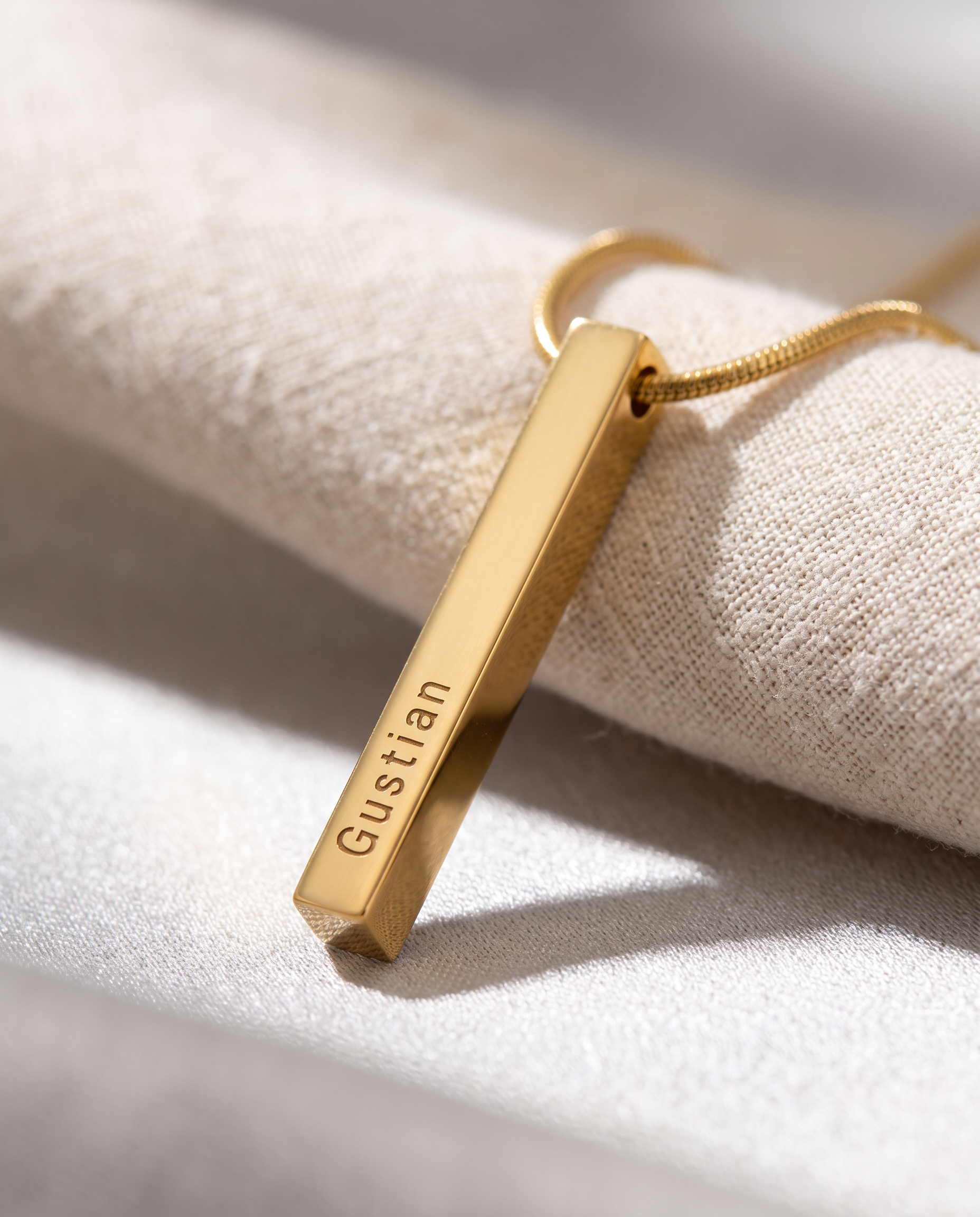 A slim vertical bar pendant with fine engraved lines running down its length