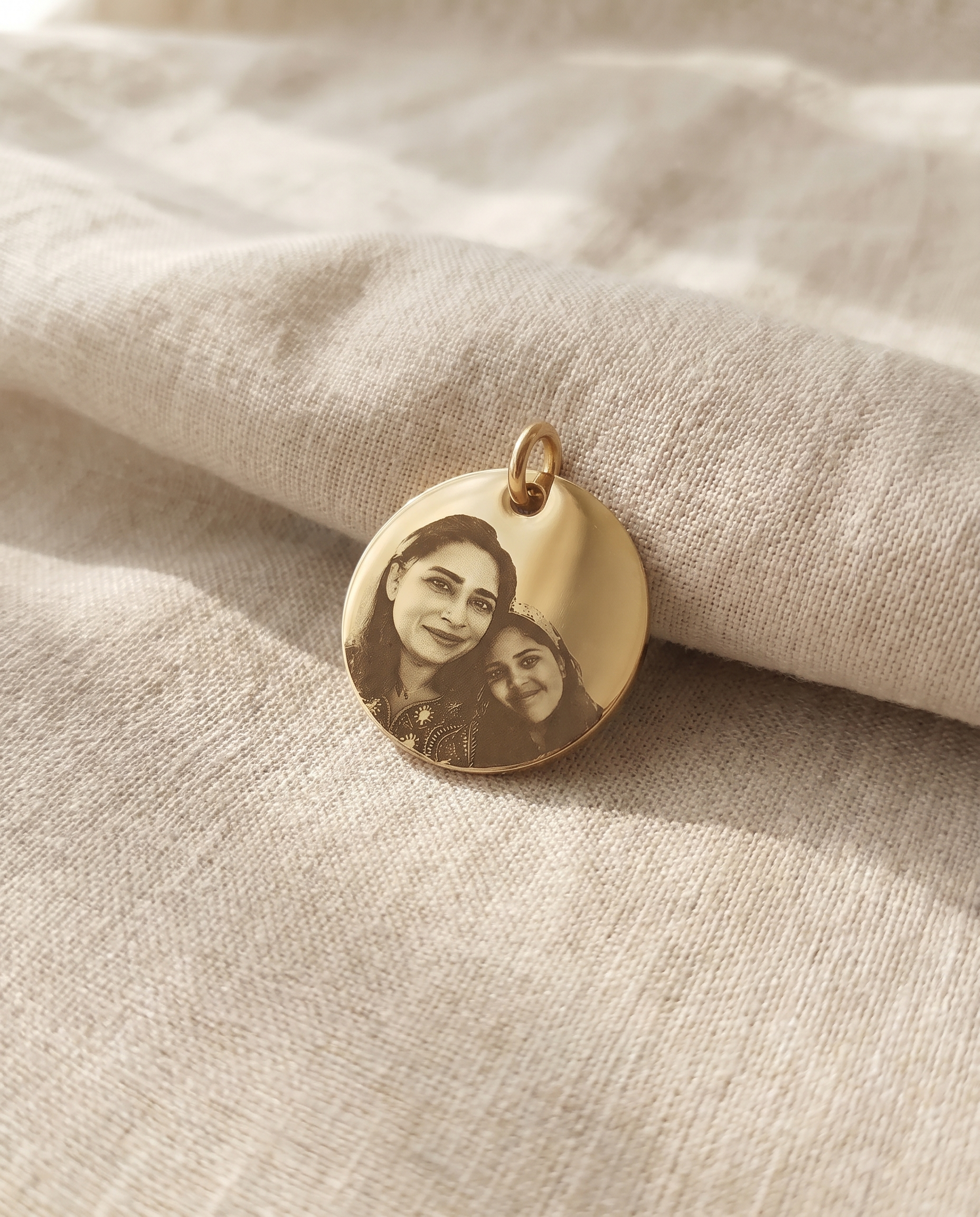 A slim engraved bar and a plain disc pendant laid side by side on linen