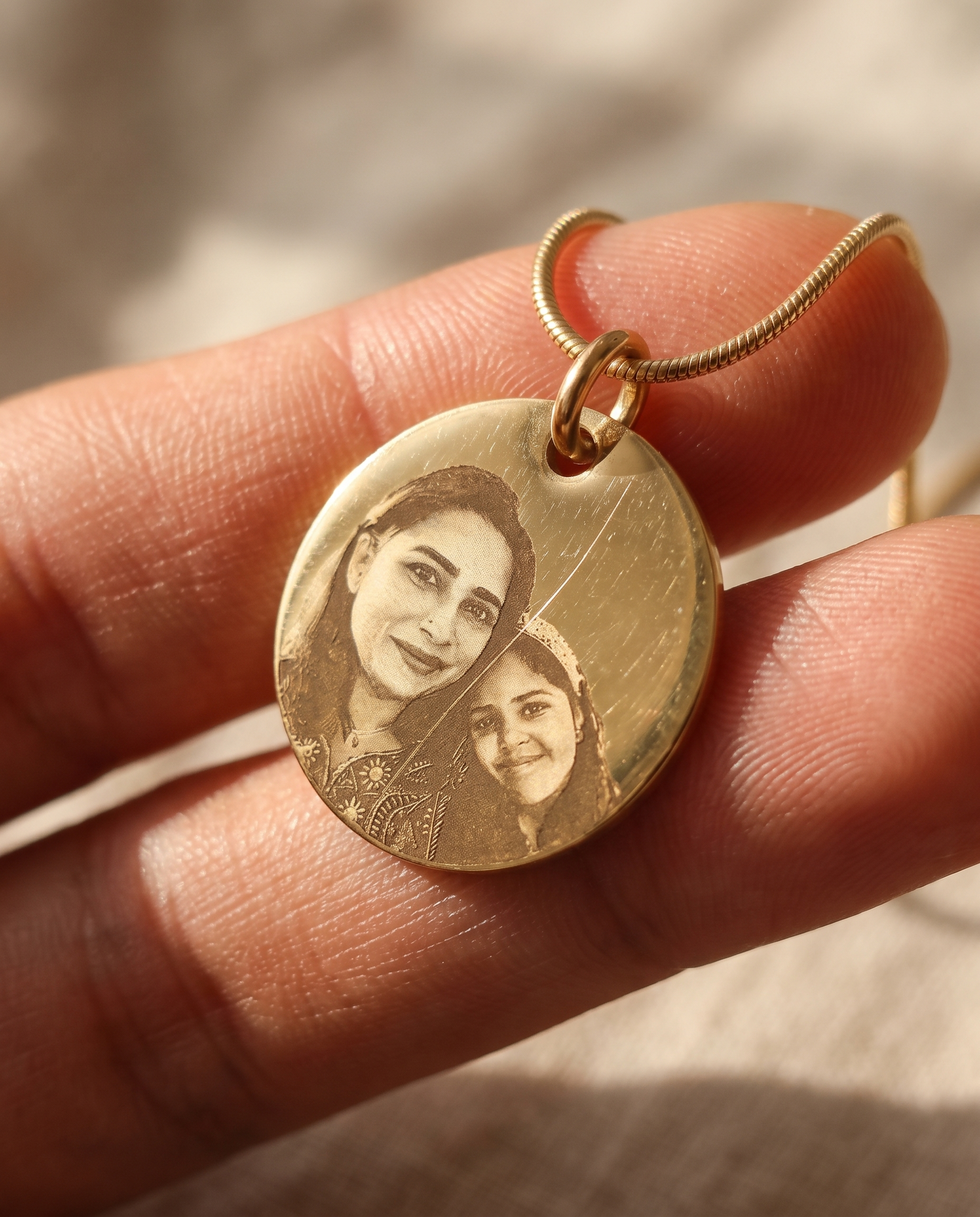A pendant held between finger and thumb, light catching the engraved line